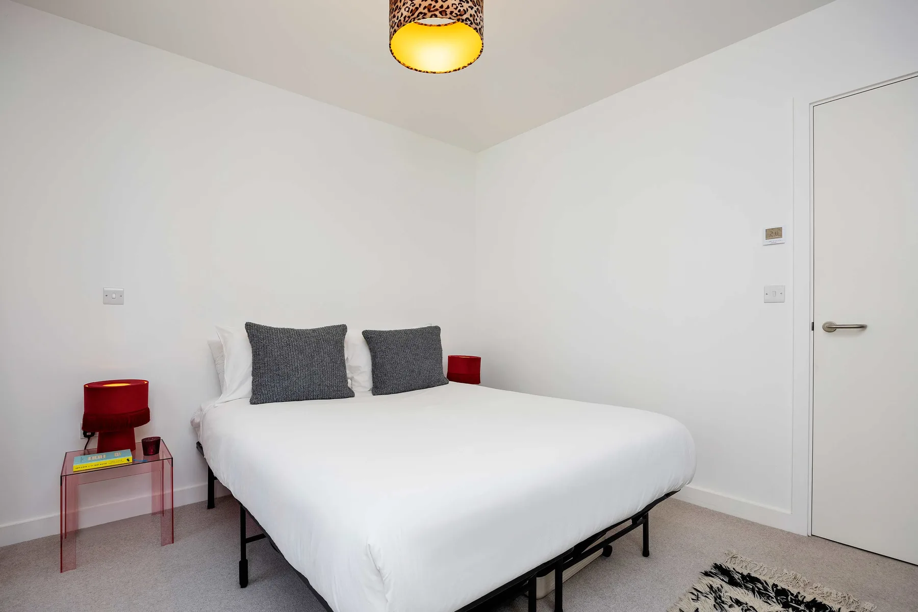 A bright bedroom with a white bed, dark pillows, and bedside tables.