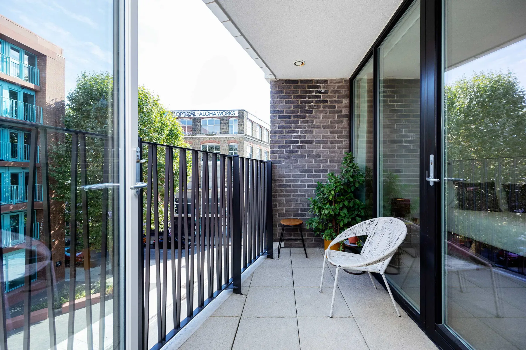 A narrow balcony with outdoor seating and a potted plant beside glass doors.