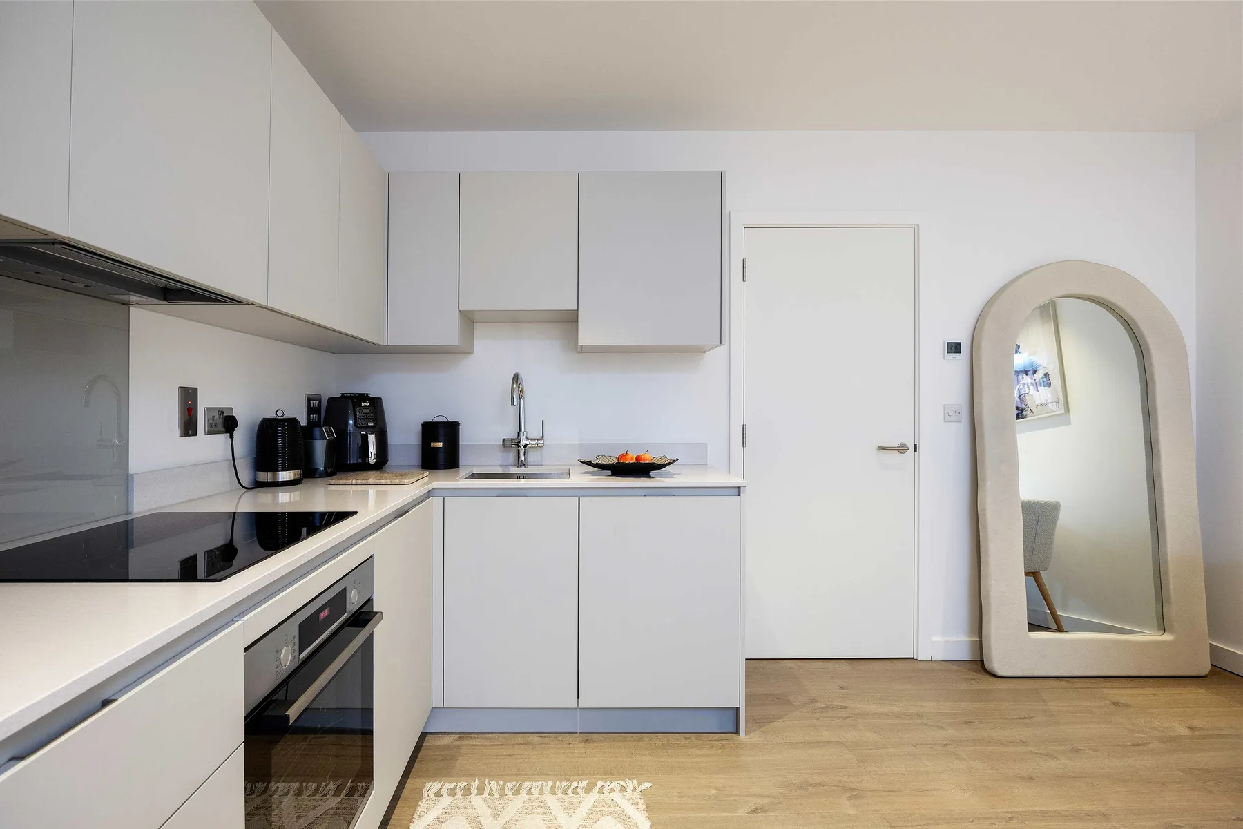 A bright modern kitchen with white cabinets, dark countertops, and a small dining area.