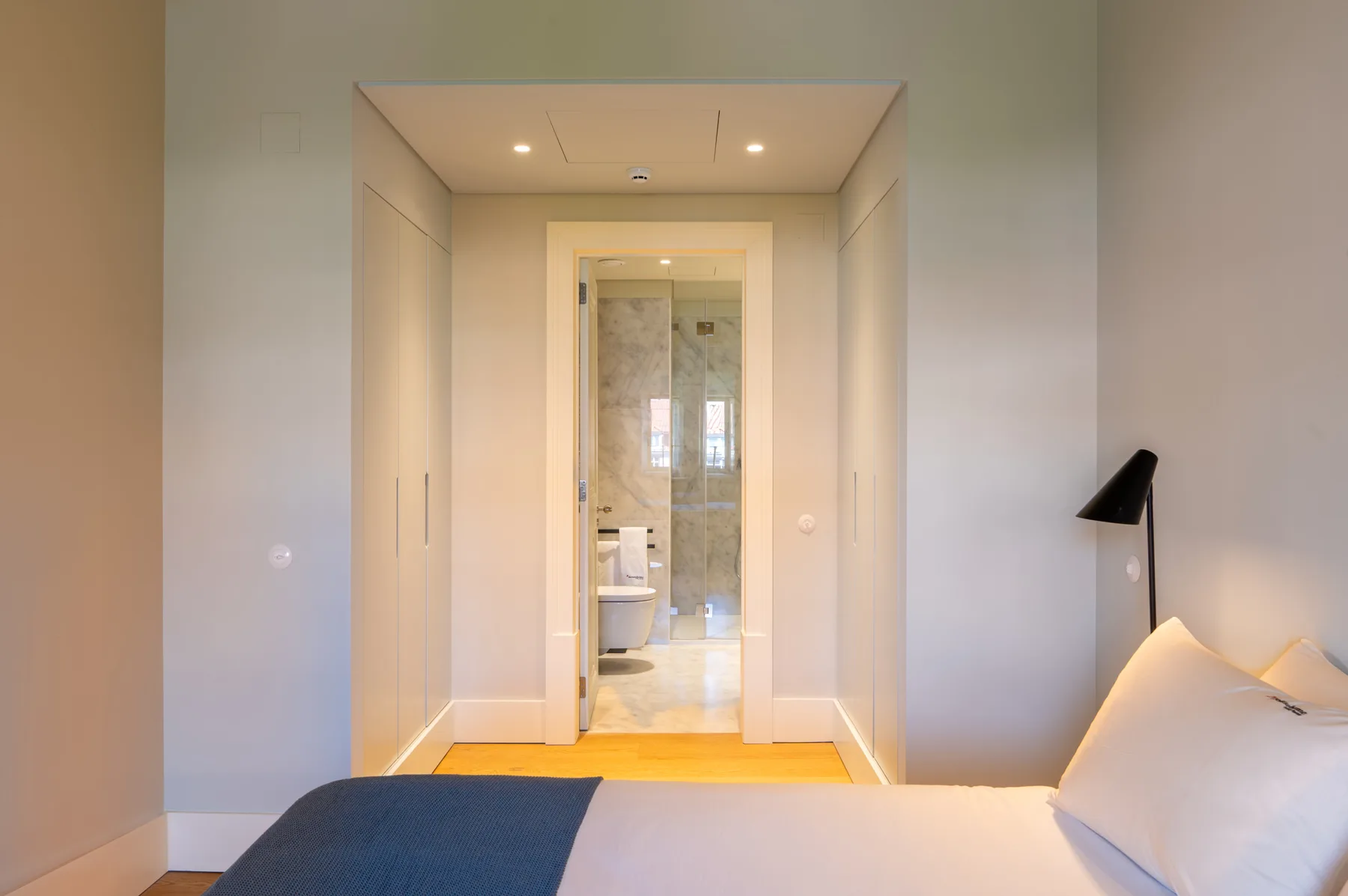 A bedroom with a bed facing an open doorway to a bathroom.