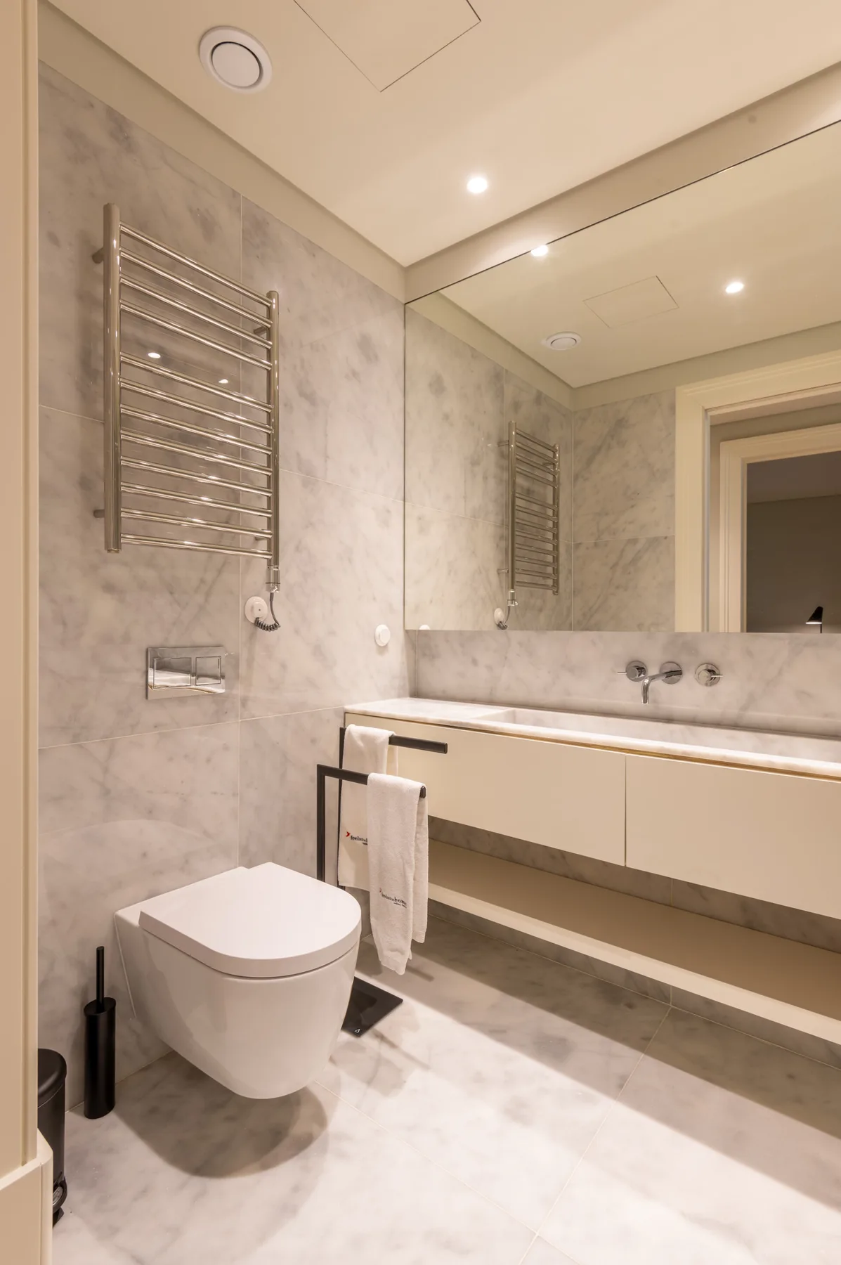 A marble-tiled bathroom with a wall-mounted toilet and a long vanity.