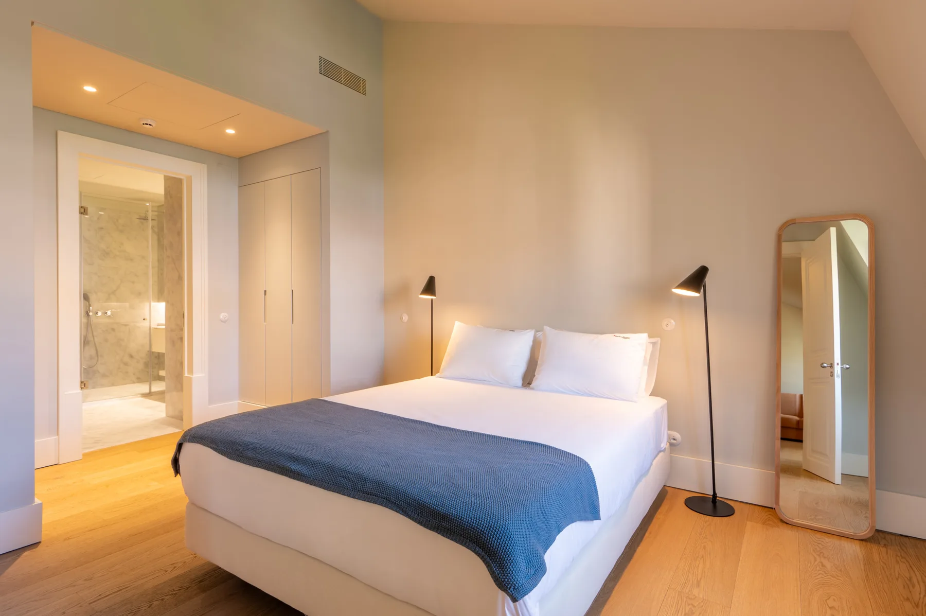 A bedroom with a bed, bedside lamps, and a full-length mirror.