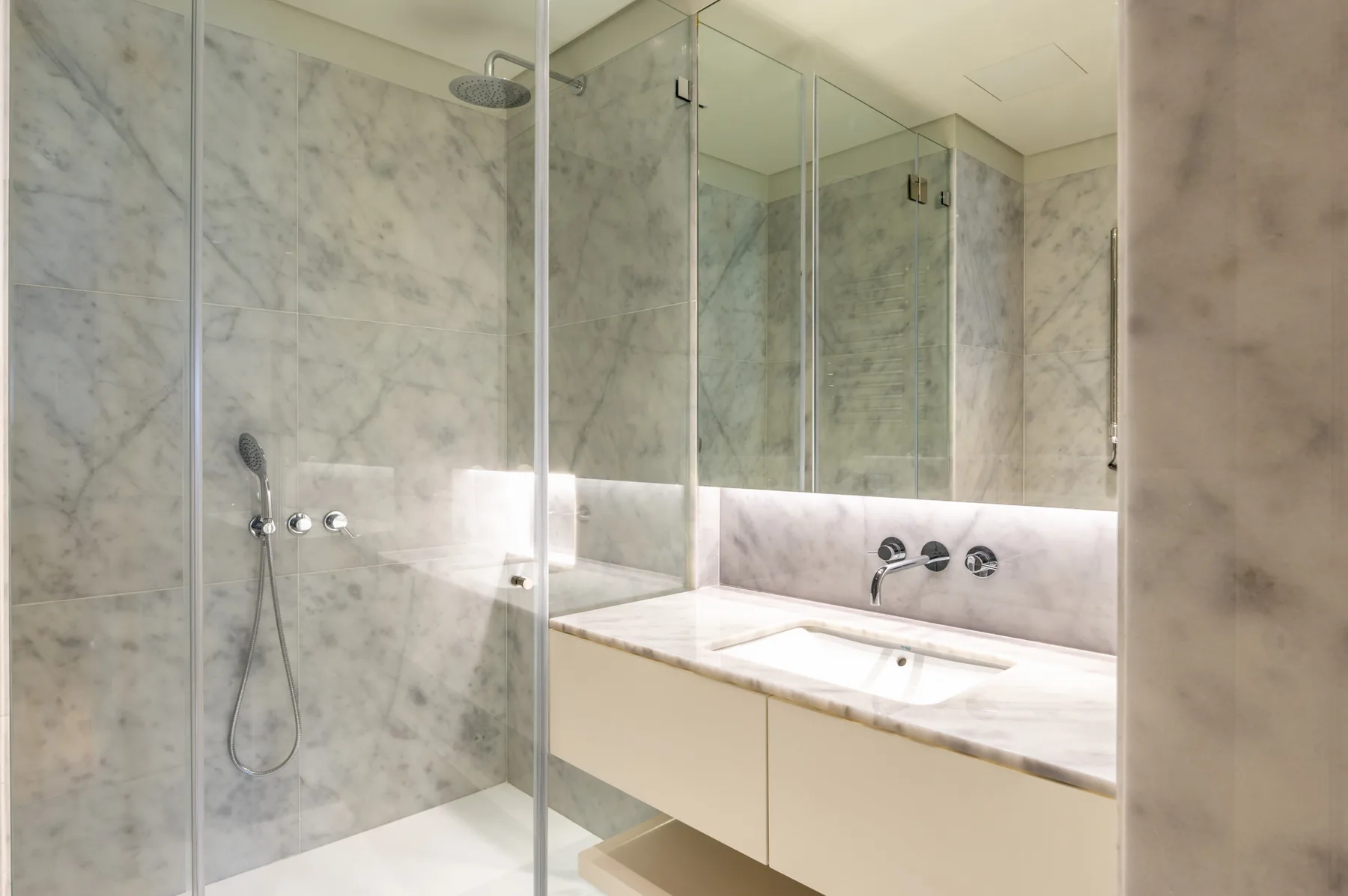 A marble bathroom with a glass shower and a wide sink counter.