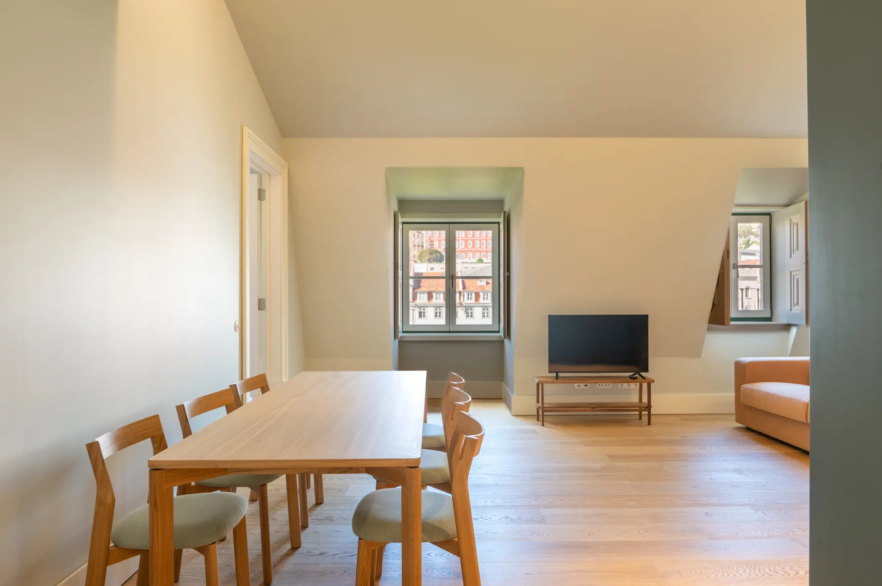 A bright living and dining room with a wooden table and television.