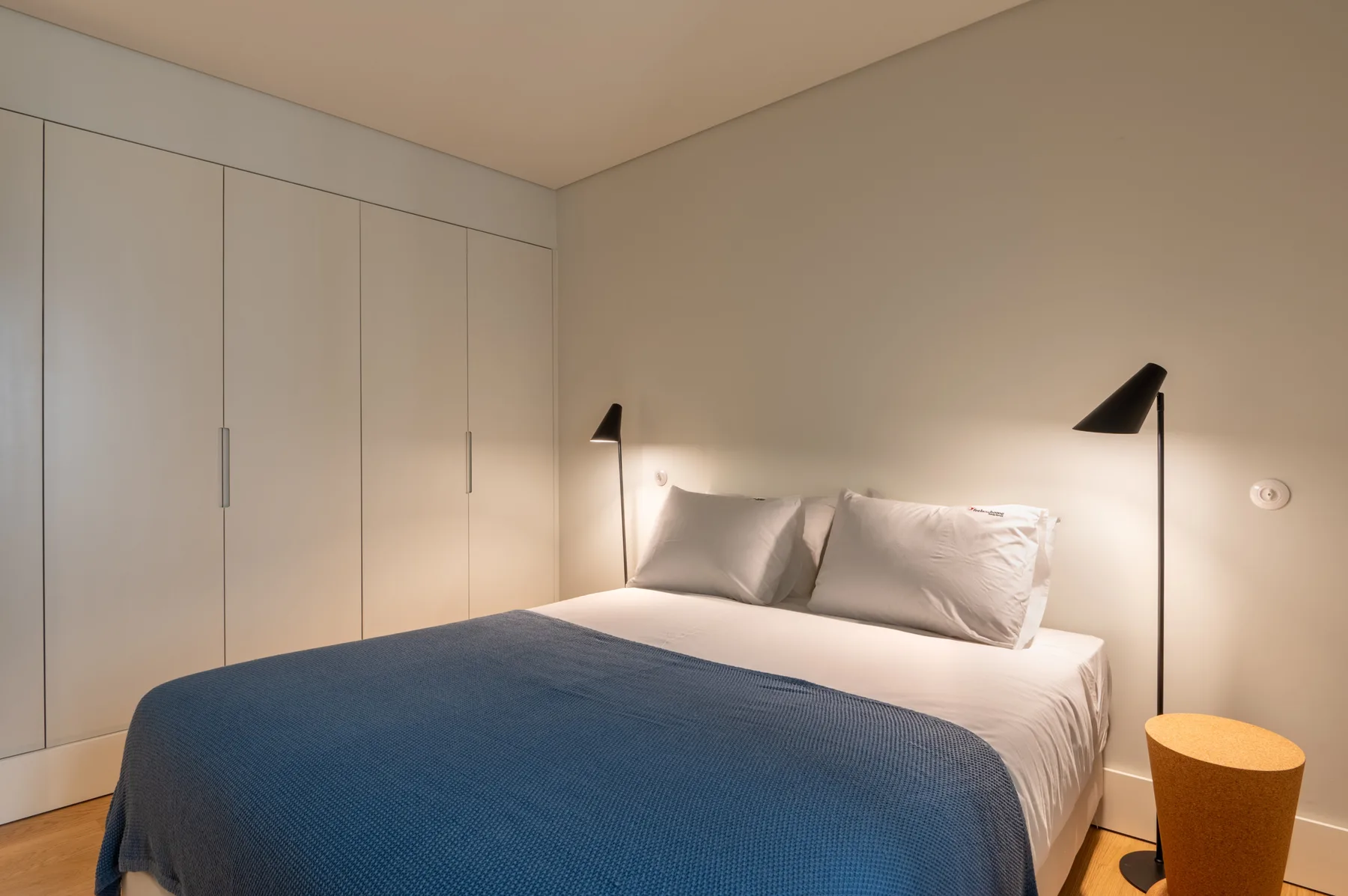 A bedroom with a bed covered by a blue blanket and bedside lamps.