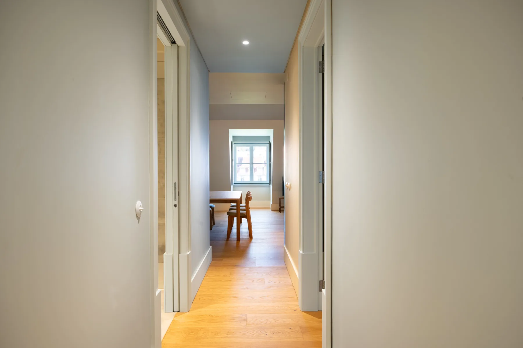 Un pasillo conduce a una zona de comedor con una ventana al fondo.