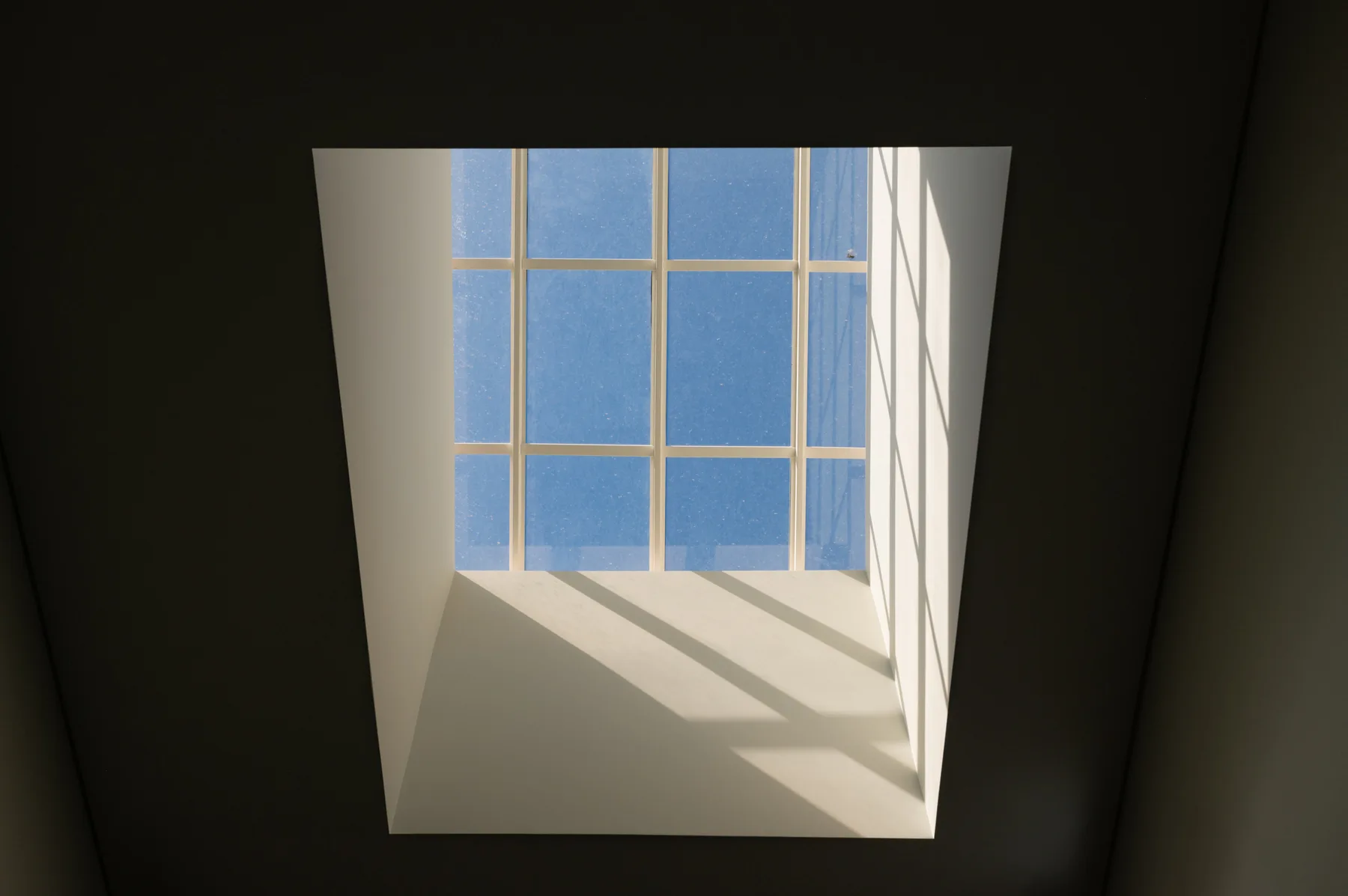 A bright skylight window casts geometric shadows across a white interior wall.