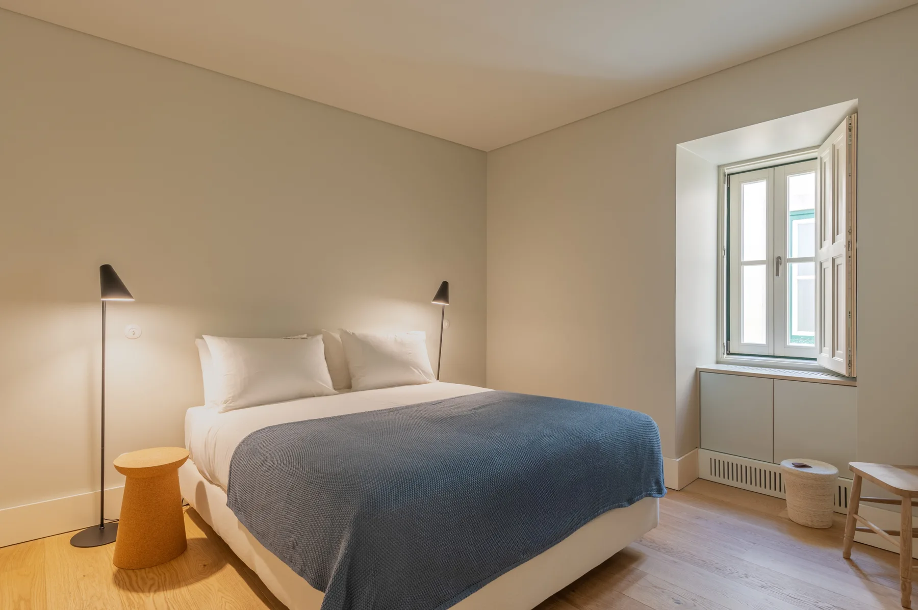 A bedroom with a bed, bedside lamps, and a window.