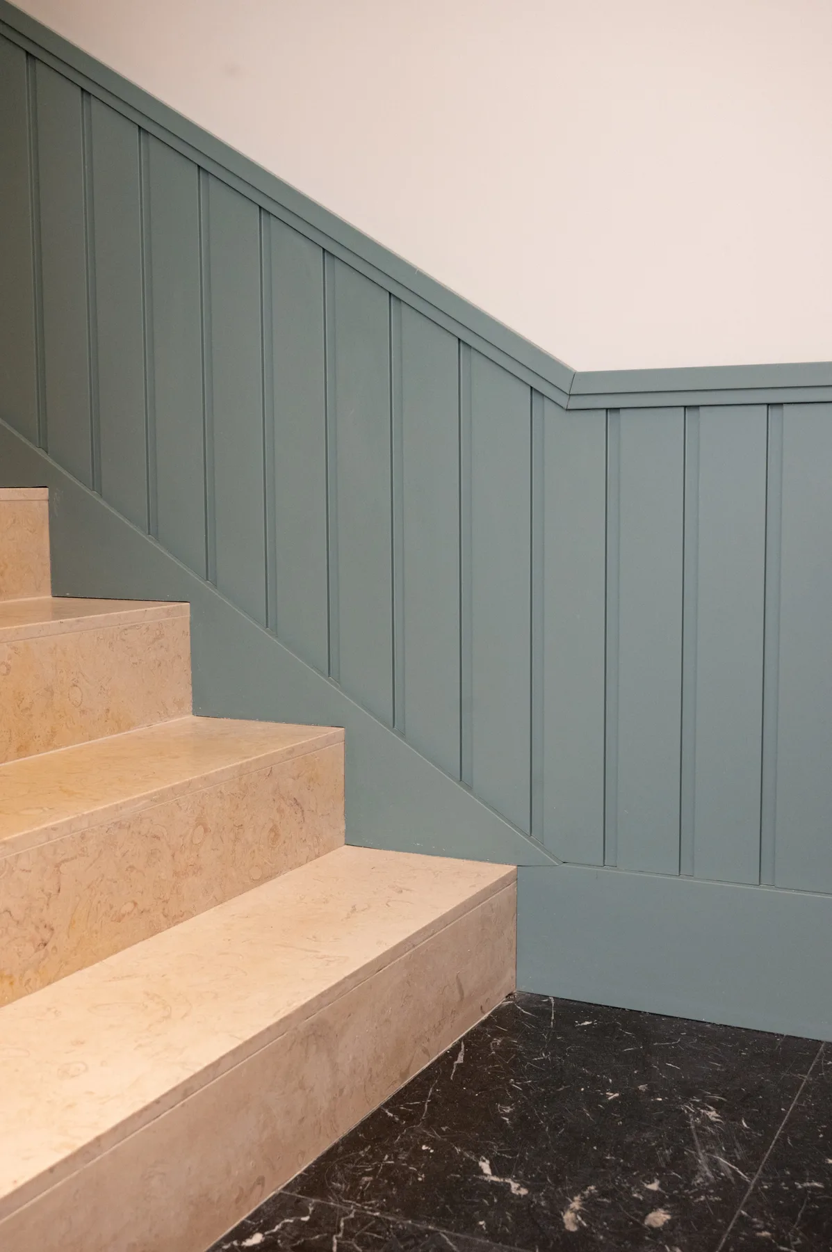 A staircase with pale stone steps and blue-gray paneled walls.