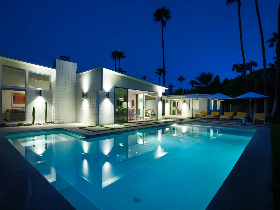 Una casa moderna y una piscina iluminada aparecen de noche.