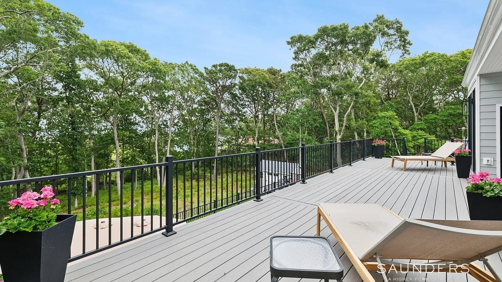 Una terraza exterior con suelo gris, barandillas negras y árboles alrededor.