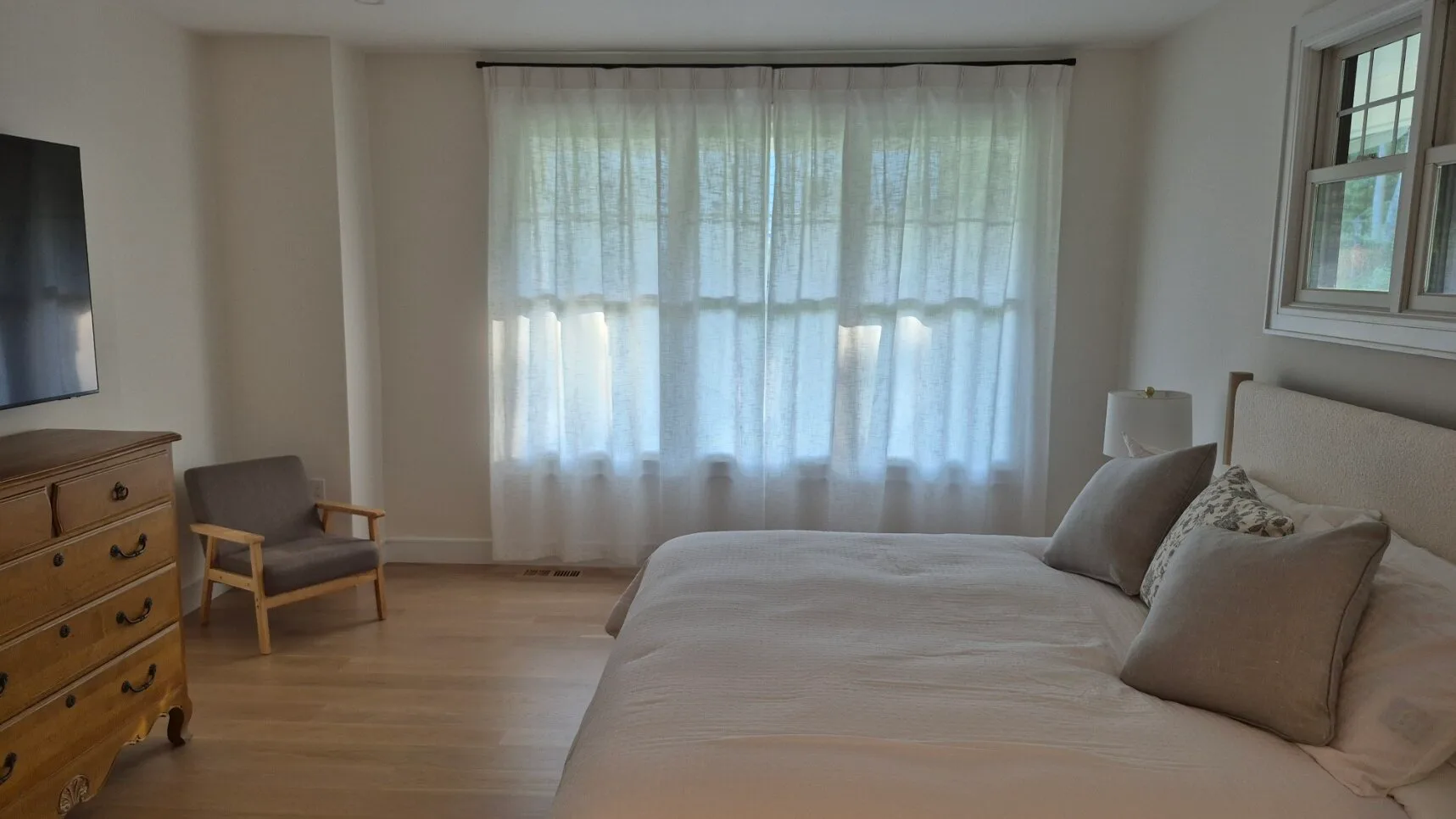 Un dormitorio con una cama grande, cortinas translúcidas y una cómoda de madera.