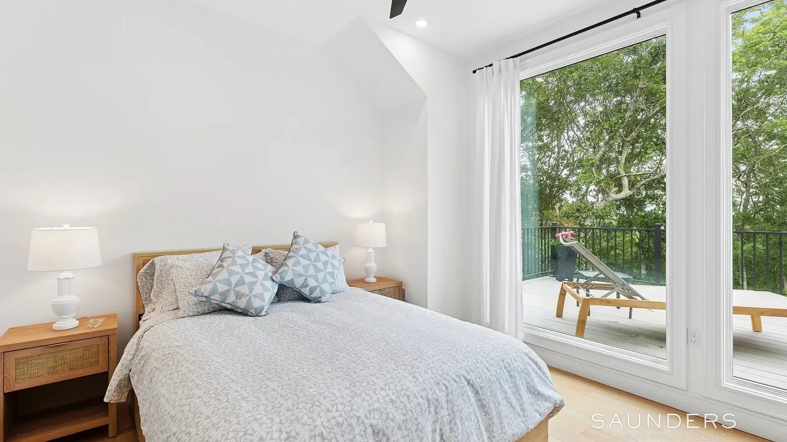 Un dormitorio luminoso con una cama bien arreglada junto a grandes ventanas con vistas a árboles frondosos.