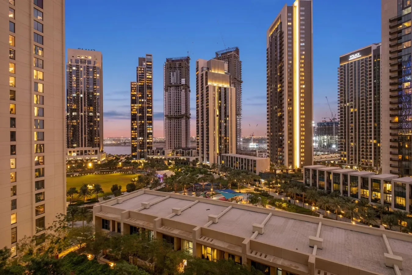 High-rise buildings surround a landscaped courtyard with a pool at dusk.