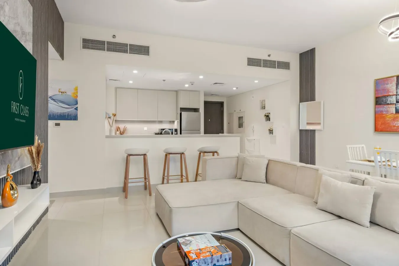 Una sala luminosa con asientos seccionales claros y una cocina abierta.
