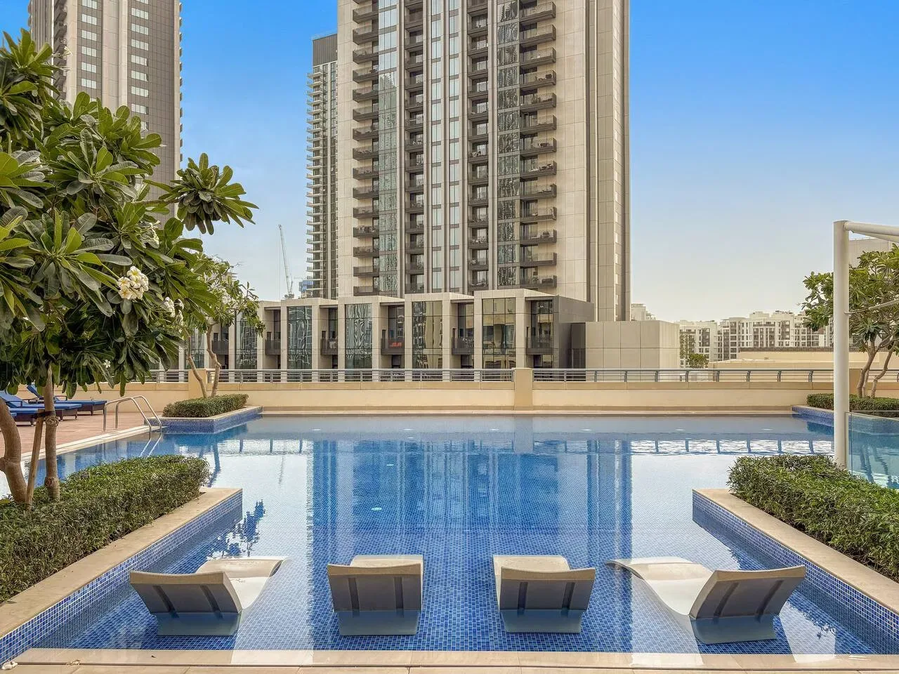 An outdoor swimming pool sits beside landscaped planters and tall residential buildings.