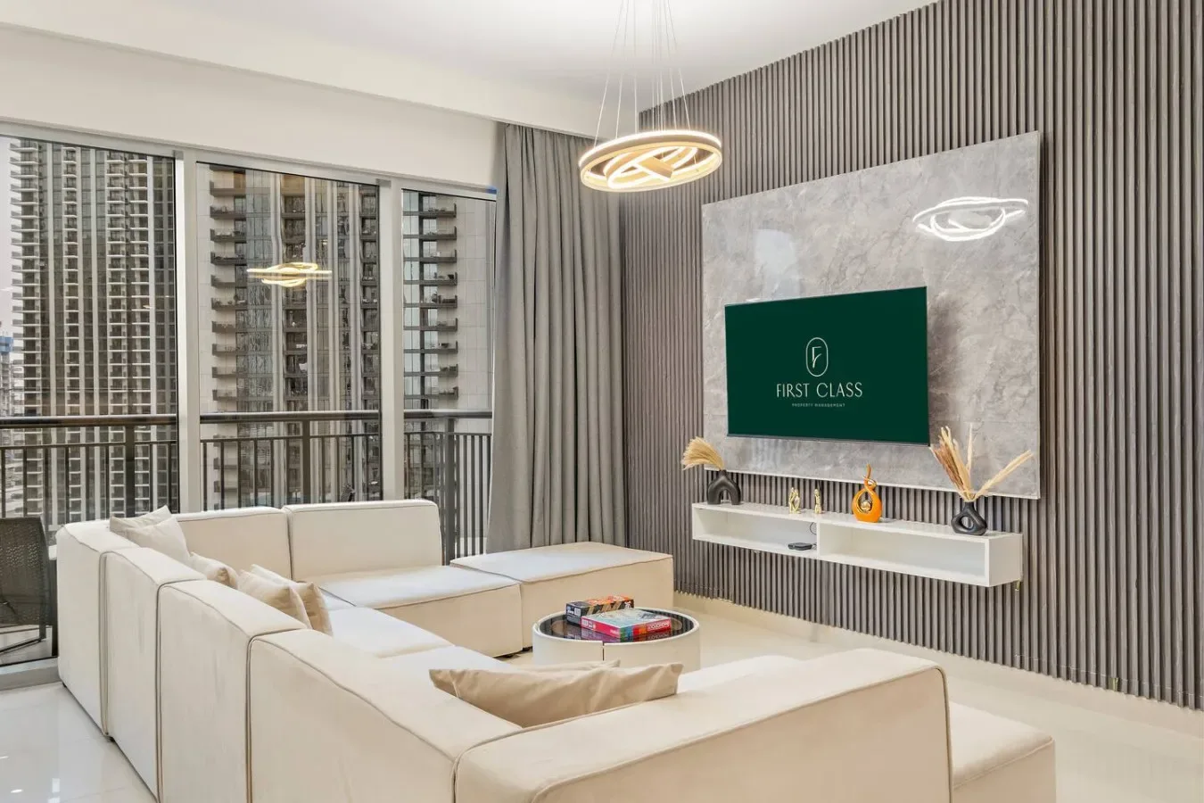 A modern living room with pale seating, large windows, and a wall-mounted television.