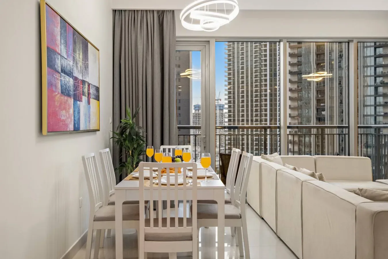 A bright dining and living area features a table beside large windows.