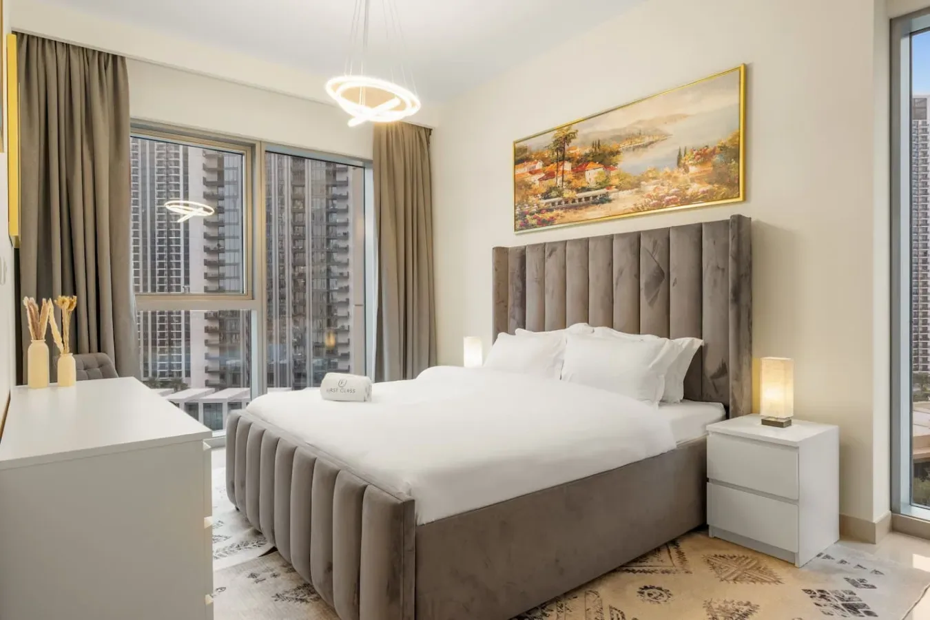 A bedroom with a large bed, upholstered headboard, and tall windows.