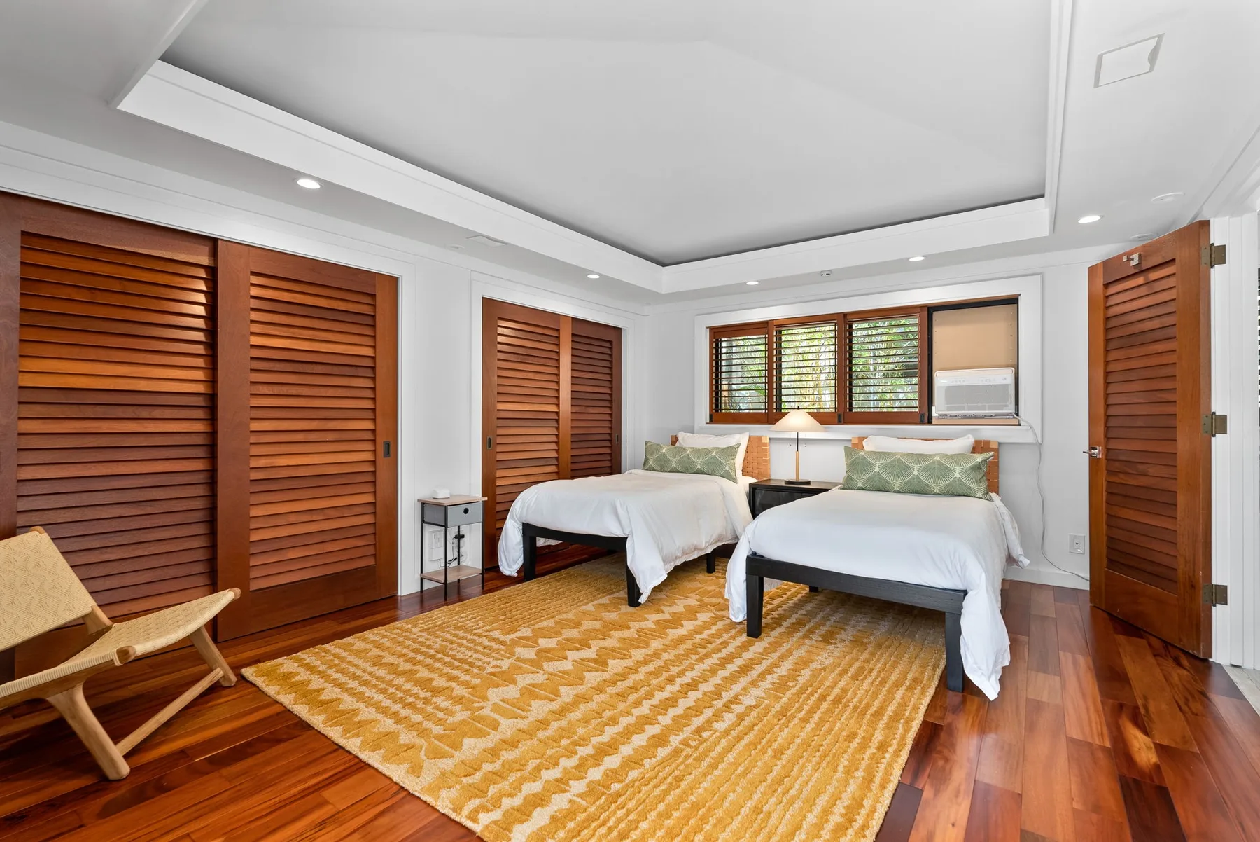 A bright bedroom with two beds, wooden shutters, and a patterned rug.
