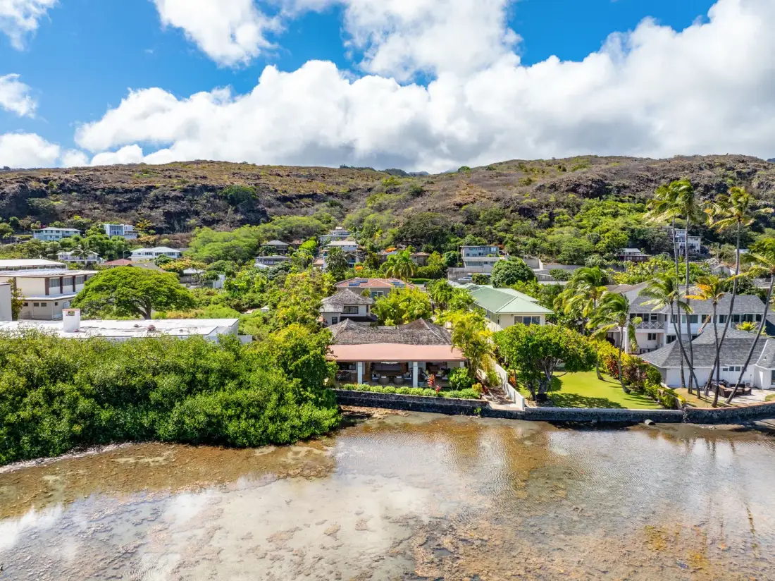 A coastal neighborhood of homes and greenery sits beside shallow water.