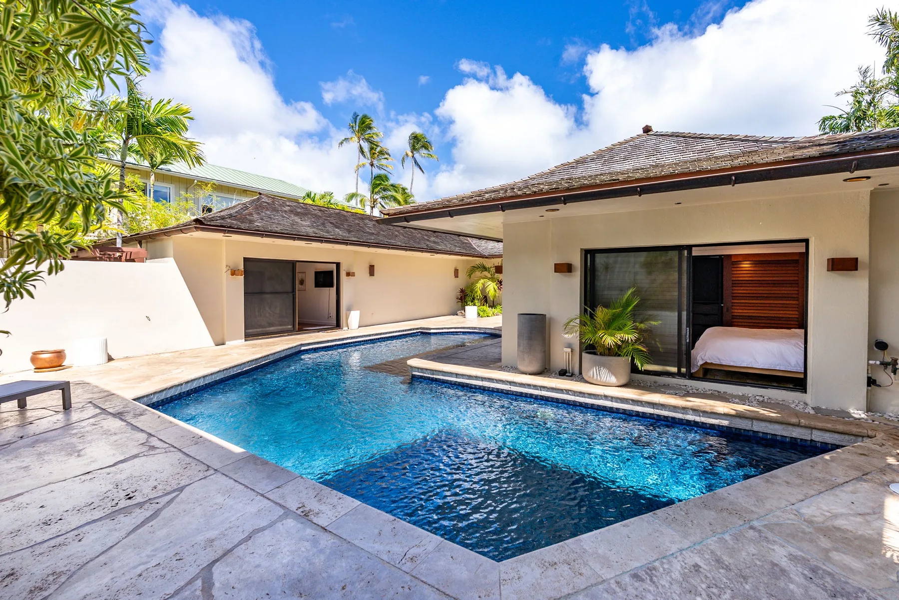 A swimming pool sits beside a low-rise building with an open bedroom.