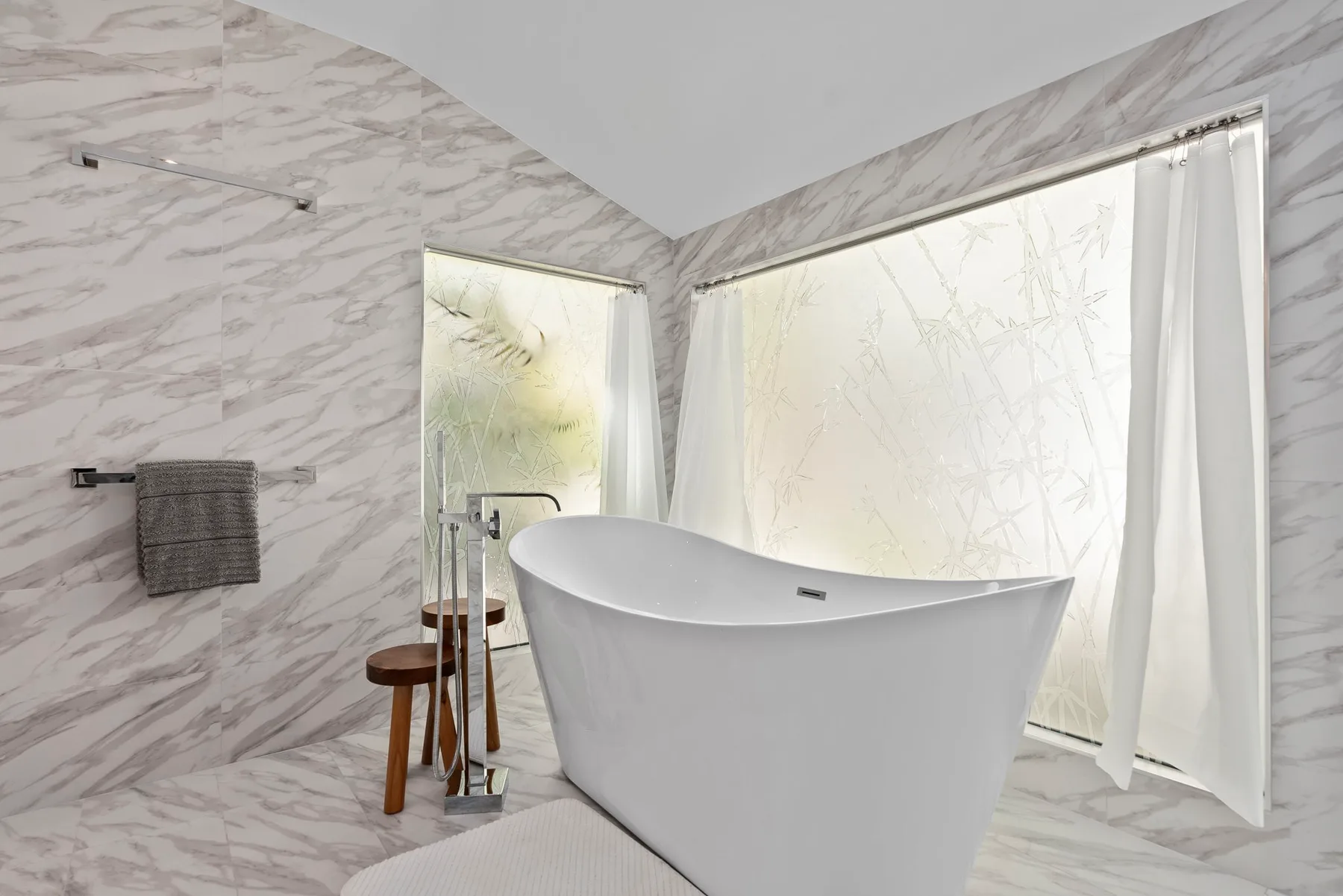 A freestanding bathtub sits beside large windows in a bright bathroom.