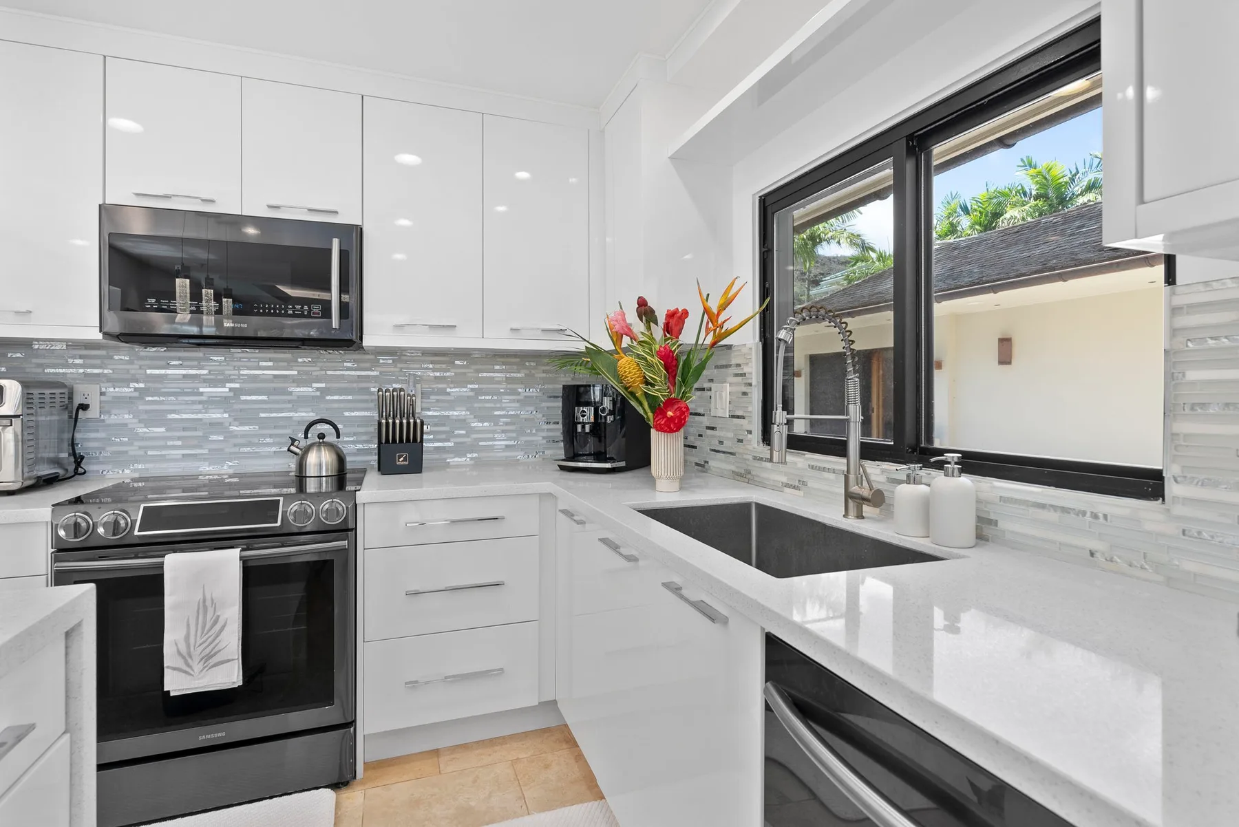 A bright modern kitchen with white cabinetry and a dark countertop range.