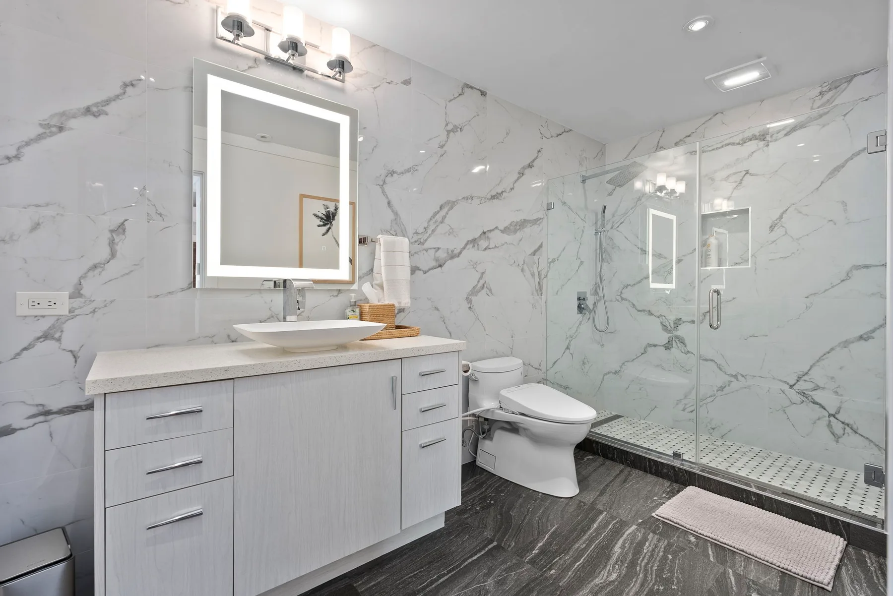 A bright bathroom with a vanity, mirror, and glass shower.