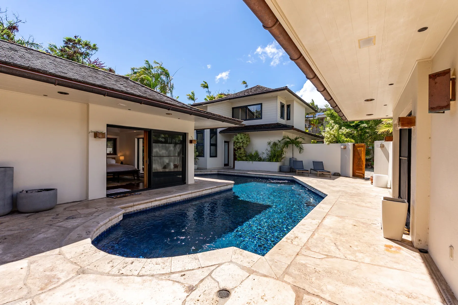 A courtyard pool sits beside a house, with paved walkways and outdoor seating.