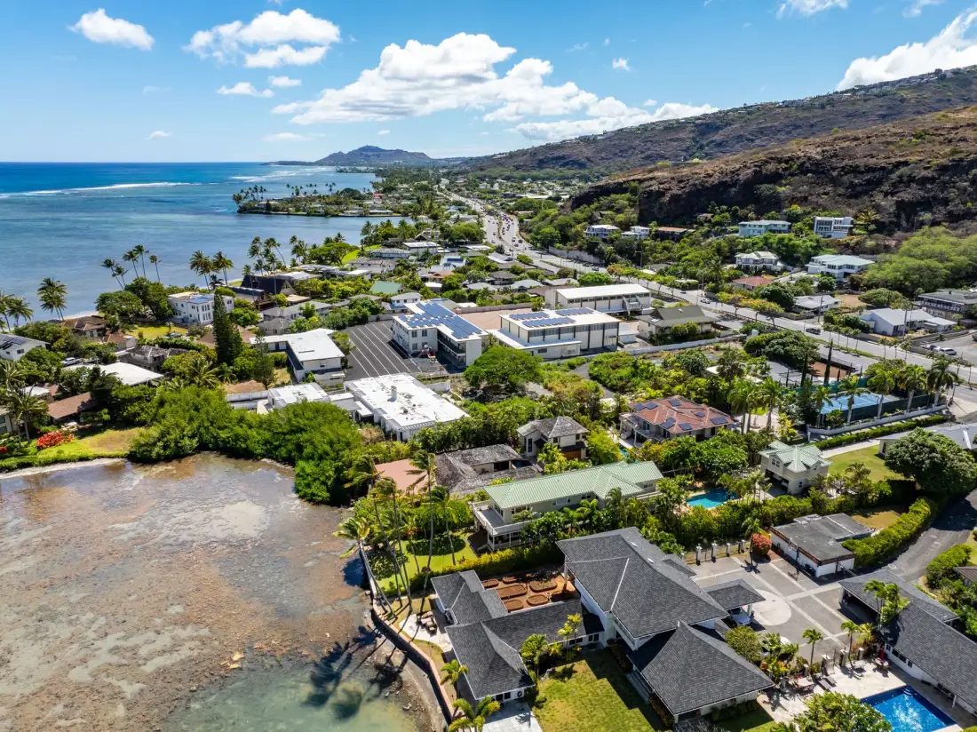 An aerial view of coastal homes and greenery beside a blue ocean.