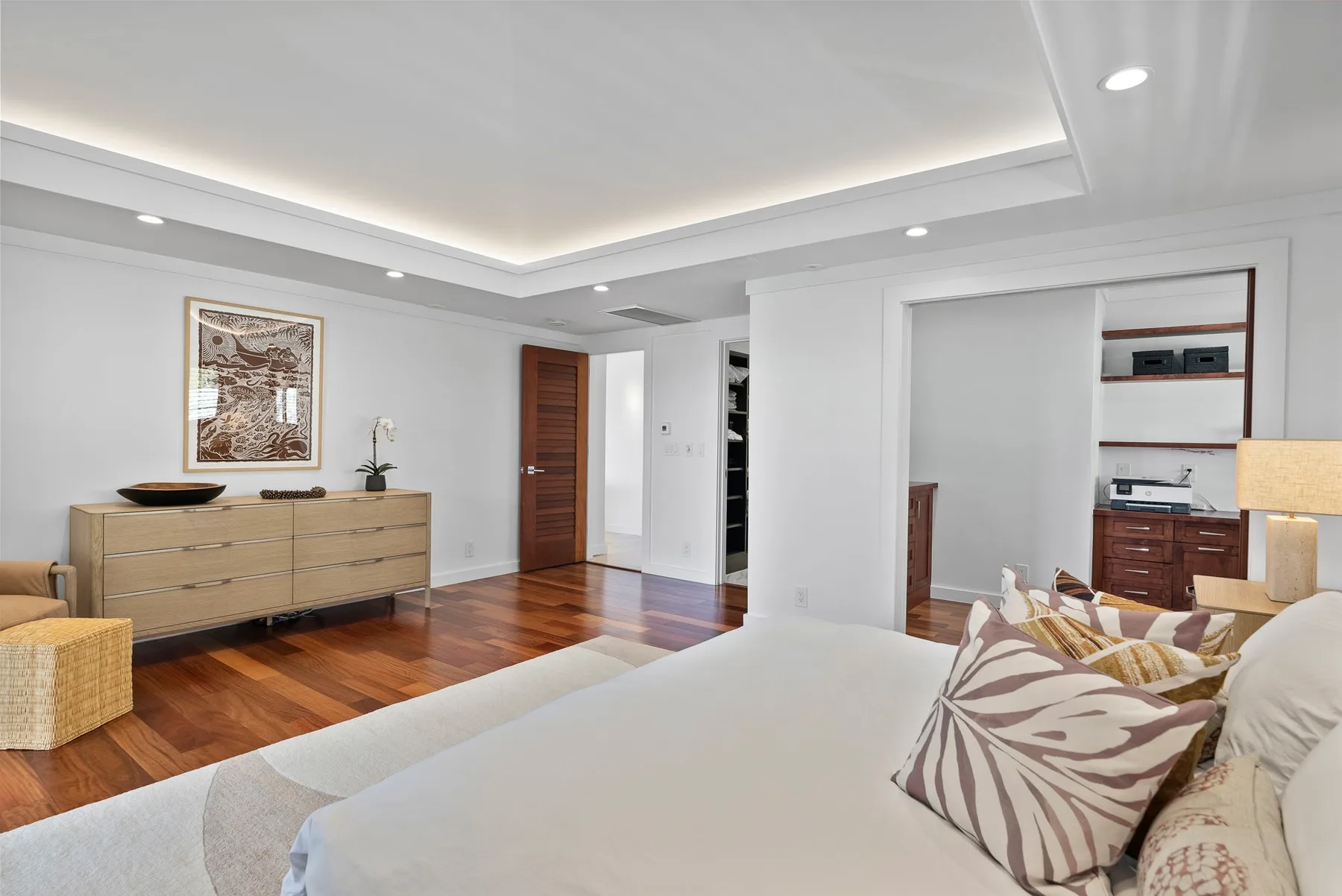 A bright bedroom with a large bed, wood flooring, and built-in storage.
