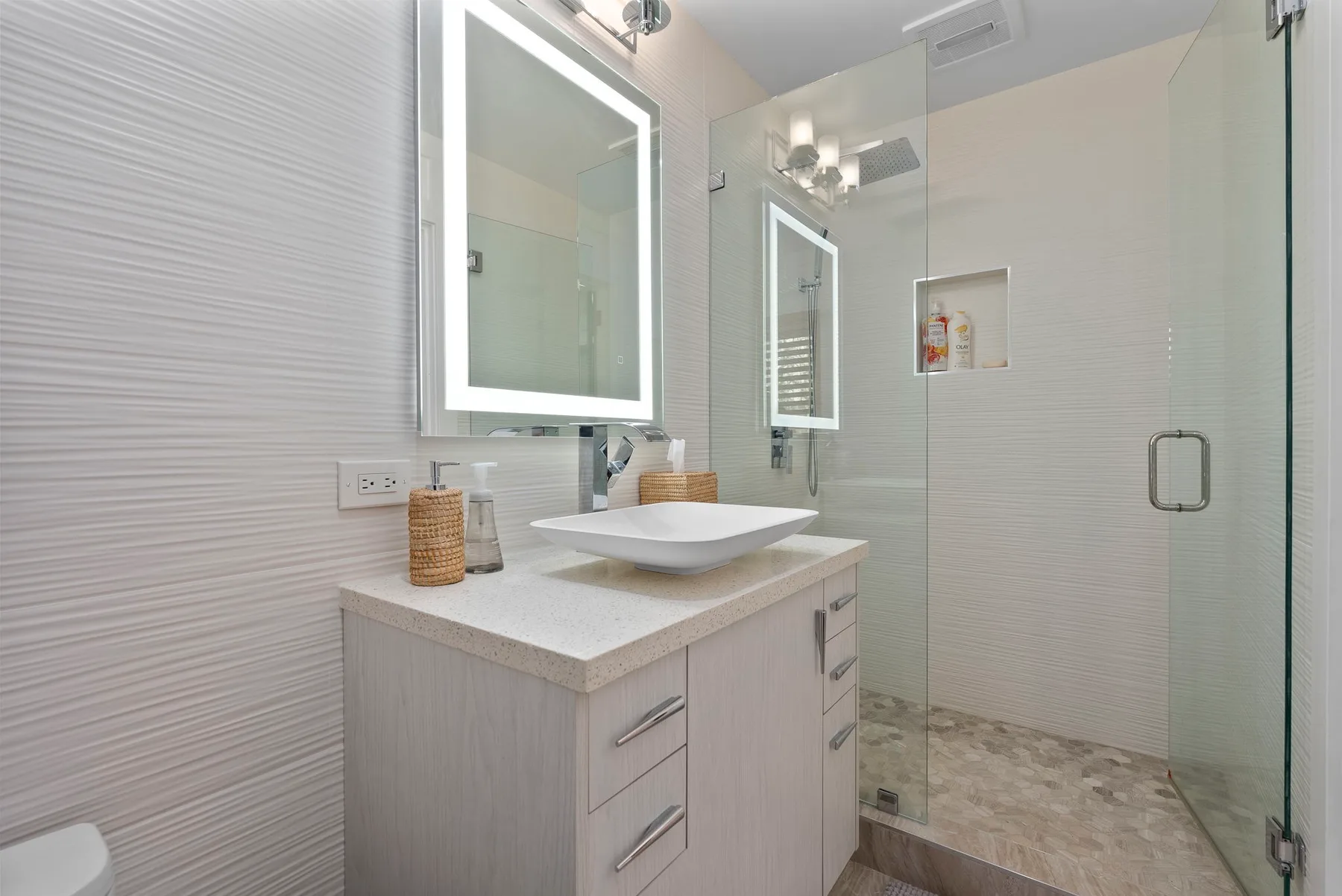 A modern bathroom with a vanity and glass-enclosed shower.