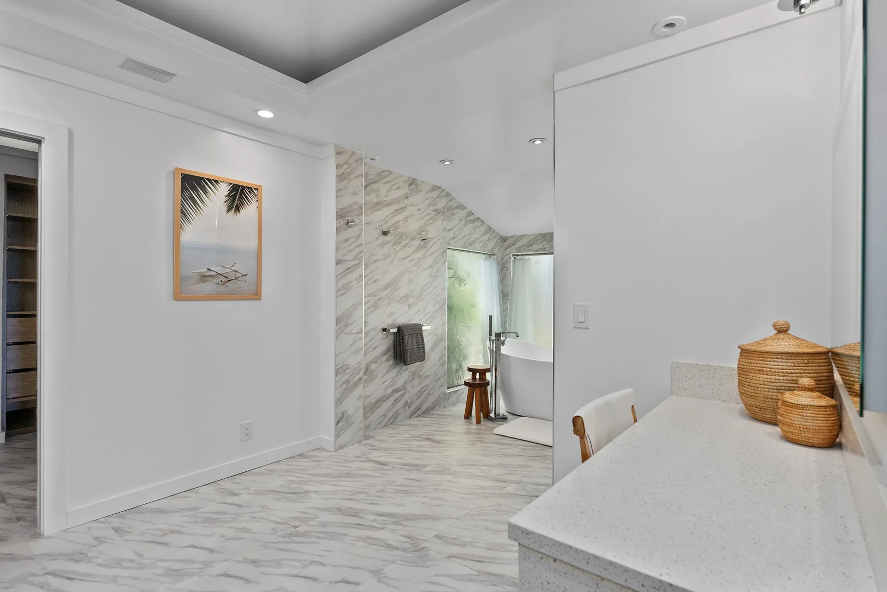A bright bathroom with a marble-patterned shower and a long countertop.