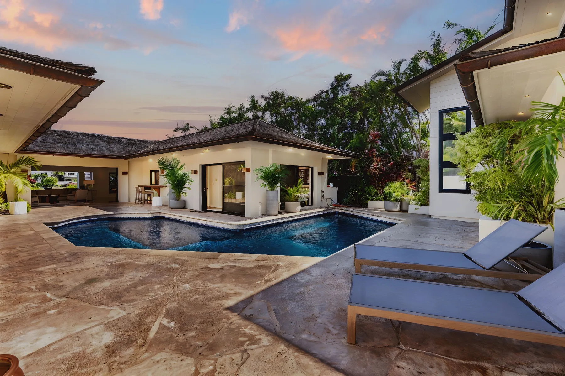 A swimming pool and lounge area sit beside a low, white villa at dusk.