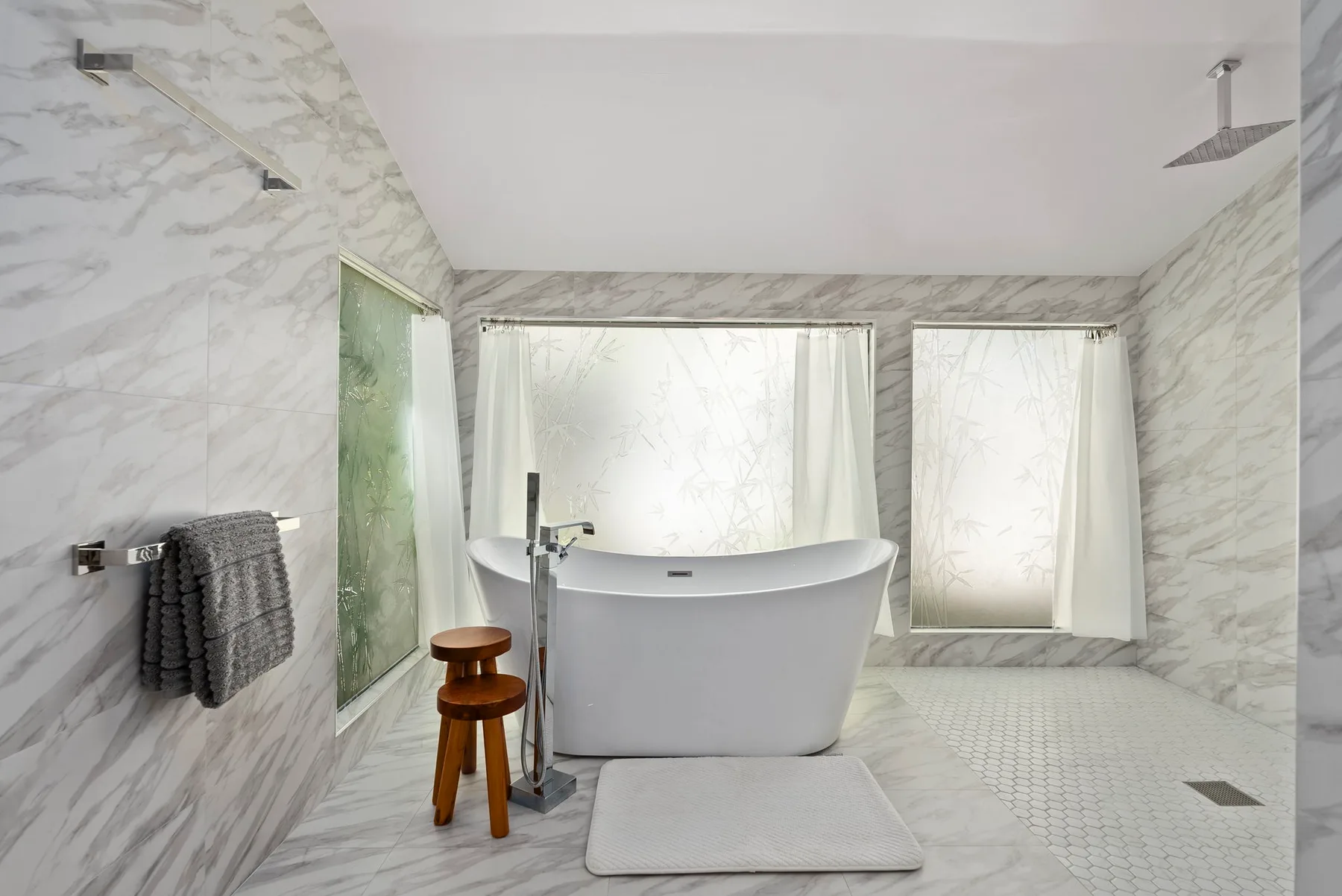 A bright bathroom features a freestanding bathtub beneath large windows.
