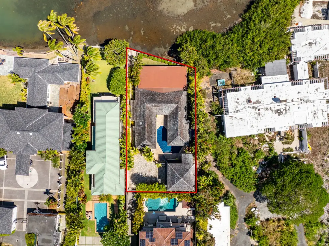 An aerial view shows a property surrounded by greenery, with a pool and nearby buildings.