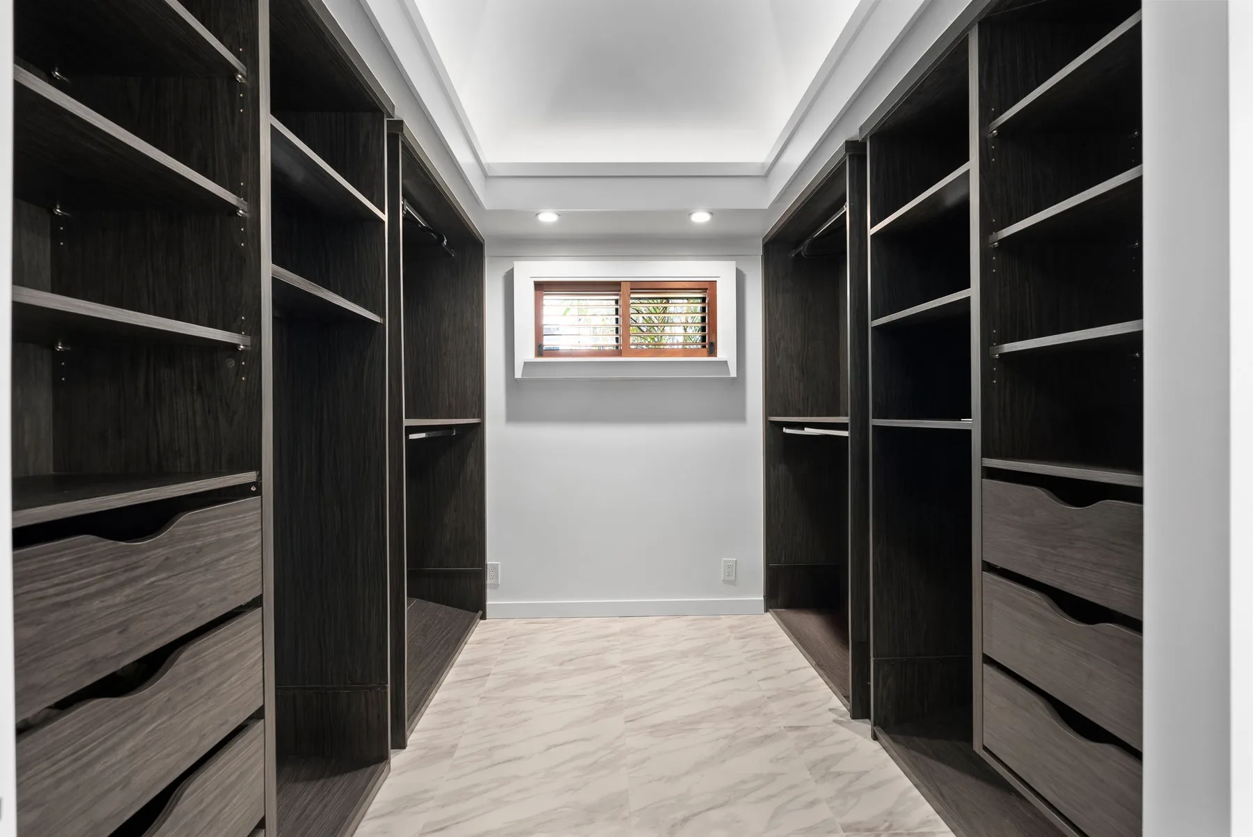 A walk-in closet with dark built-in shelving and a small window.