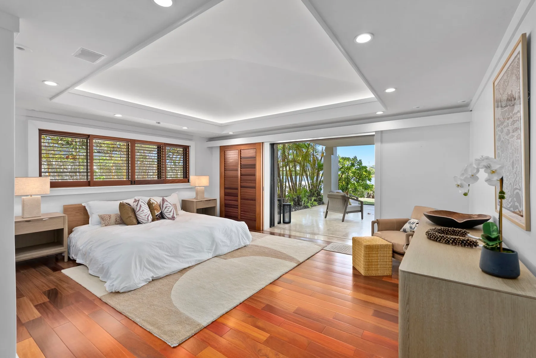 A bright bedroom with a large bed and sliding doors opening to greenery.