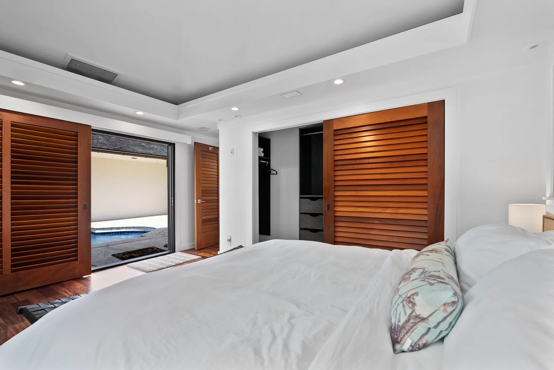 A bright bedroom with a bed beside wooden louvered closet doors.