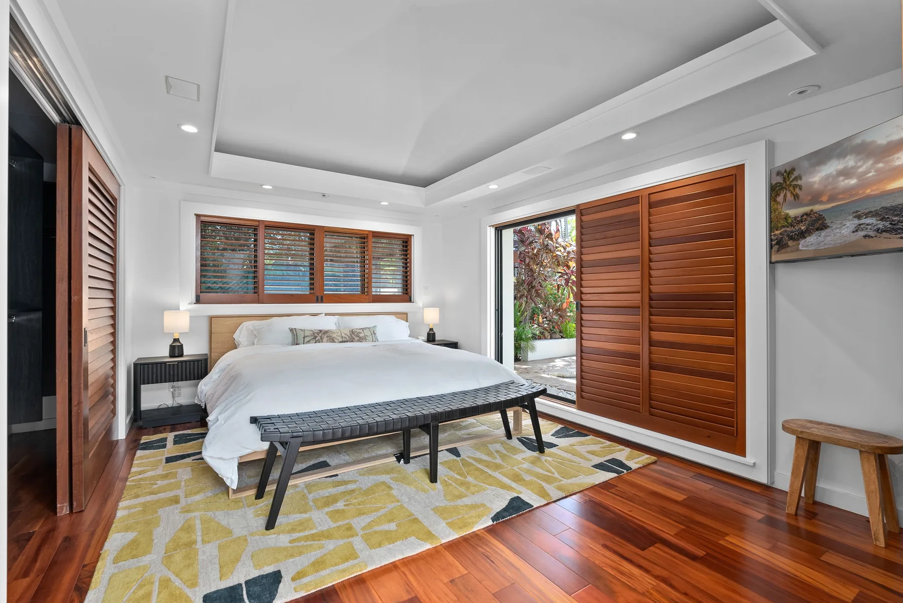A bright bedroom with a bed, wooden shutters, and a patterned rug.
