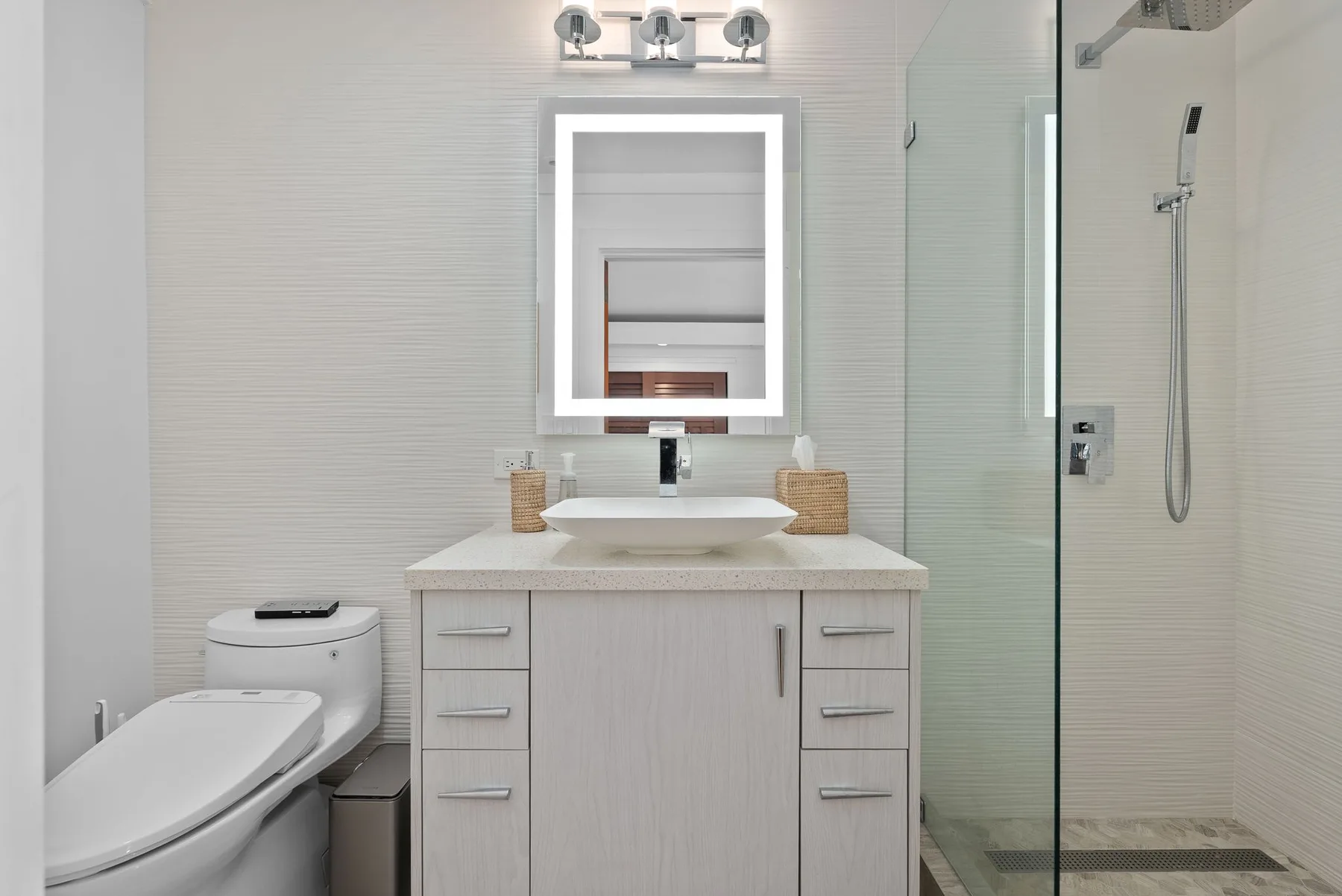 A bright bathroom with a vanity, mirror, and glass shower.