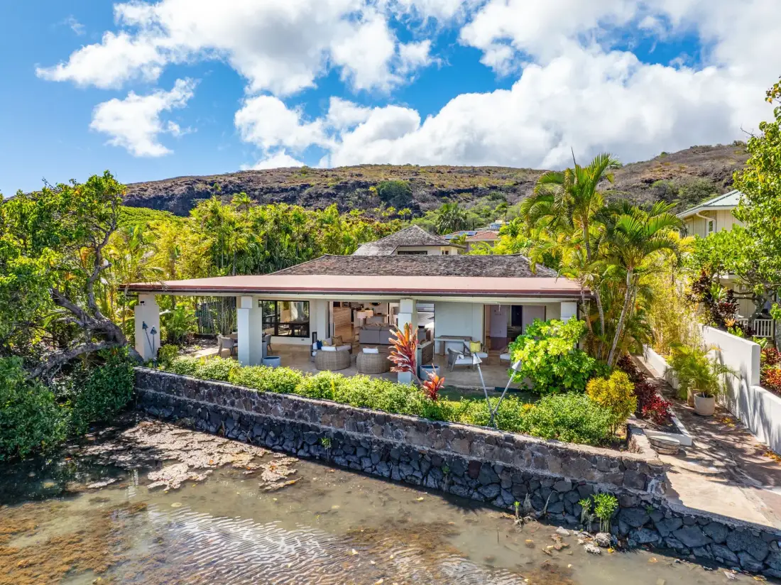 A single-story home with a covered patio overlooks a rocky shoreline.
