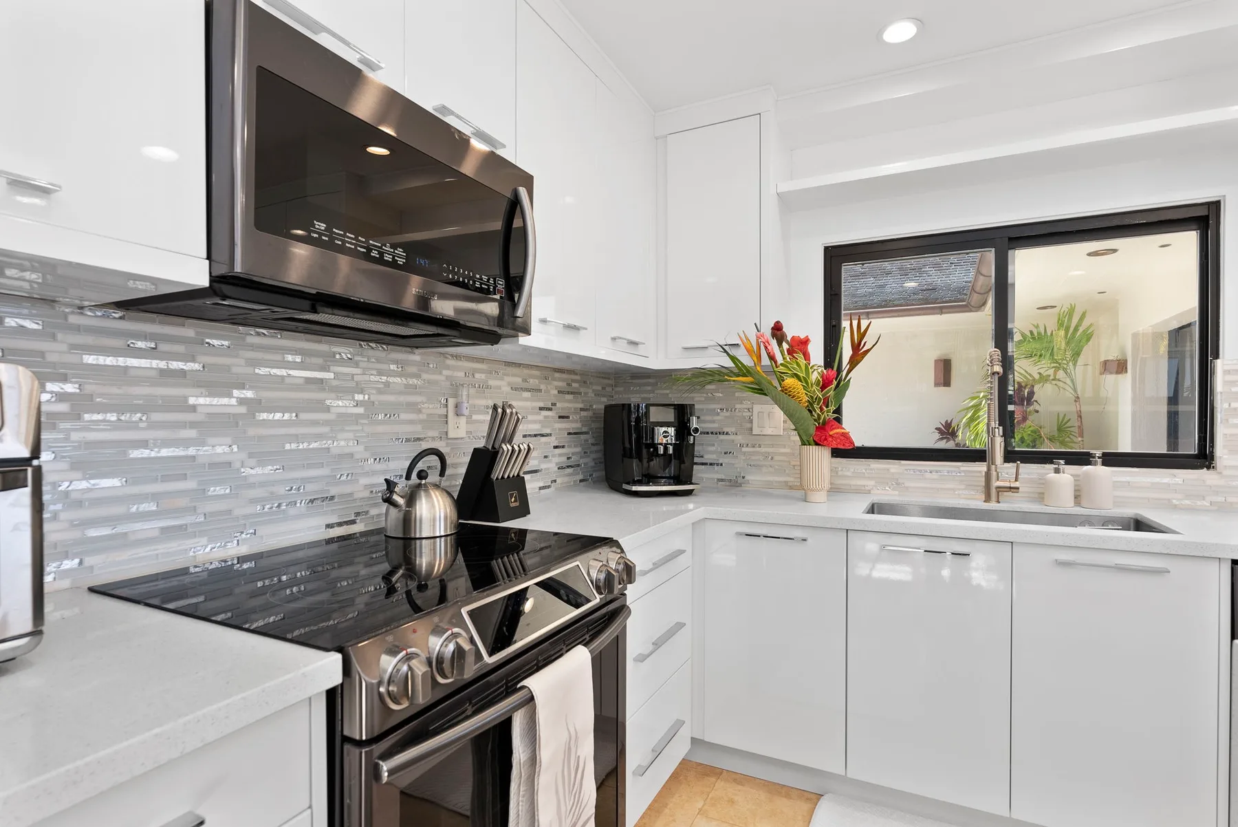 A bright kitchen with white cabinets, a stove, and a window above the sink.