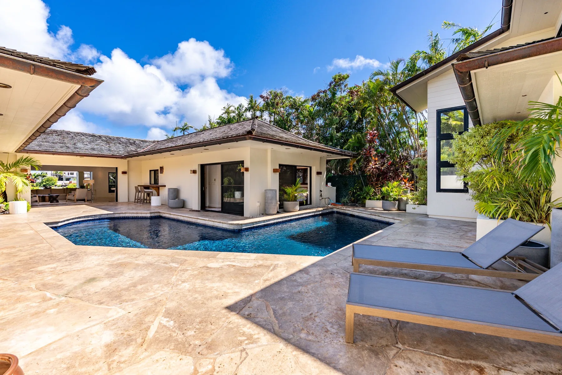 A swimming pool sits beside a modern home, with lounge chairs on the patio.