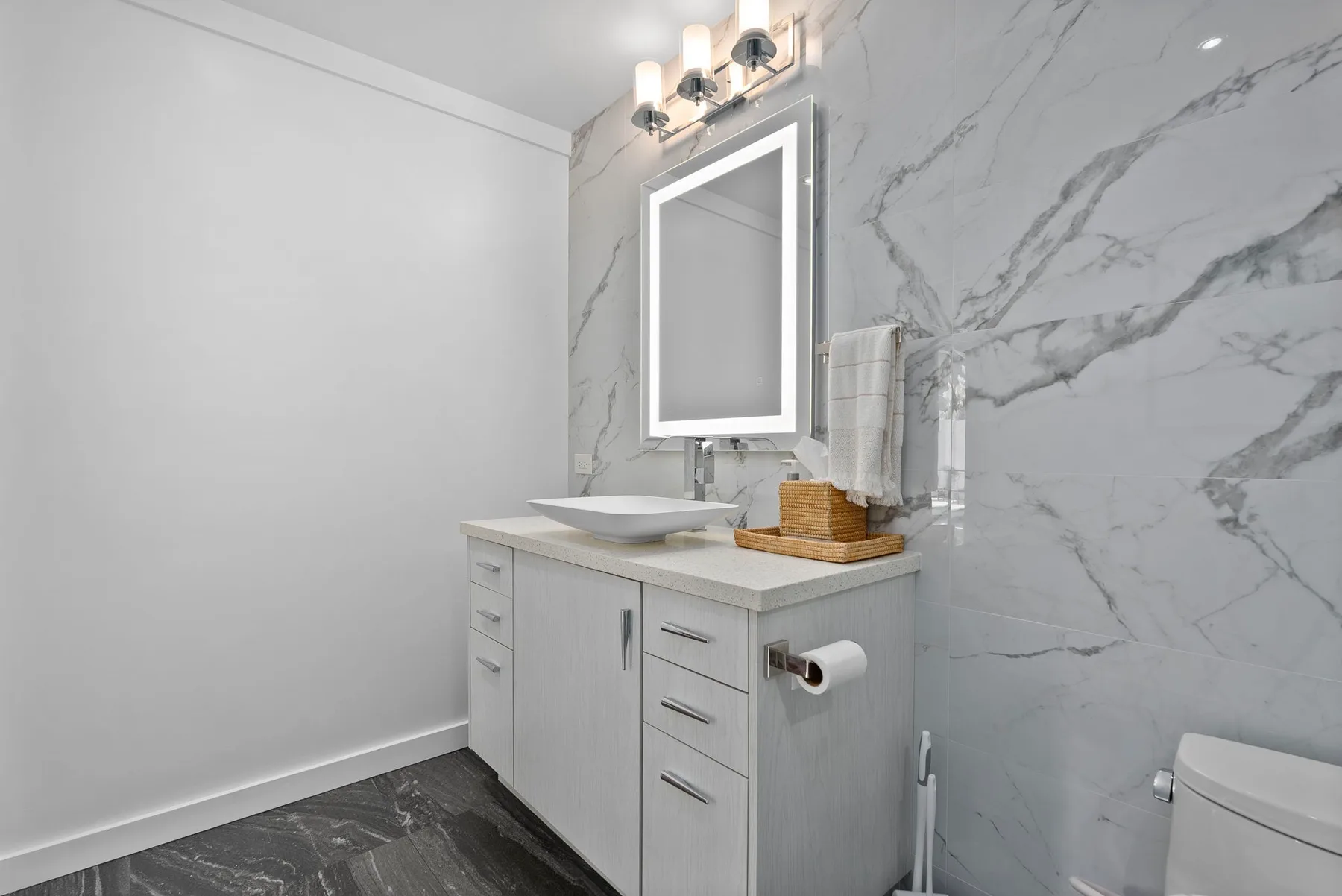 A bathroom vanity with a basin and illuminated mirror against a tiled wall.