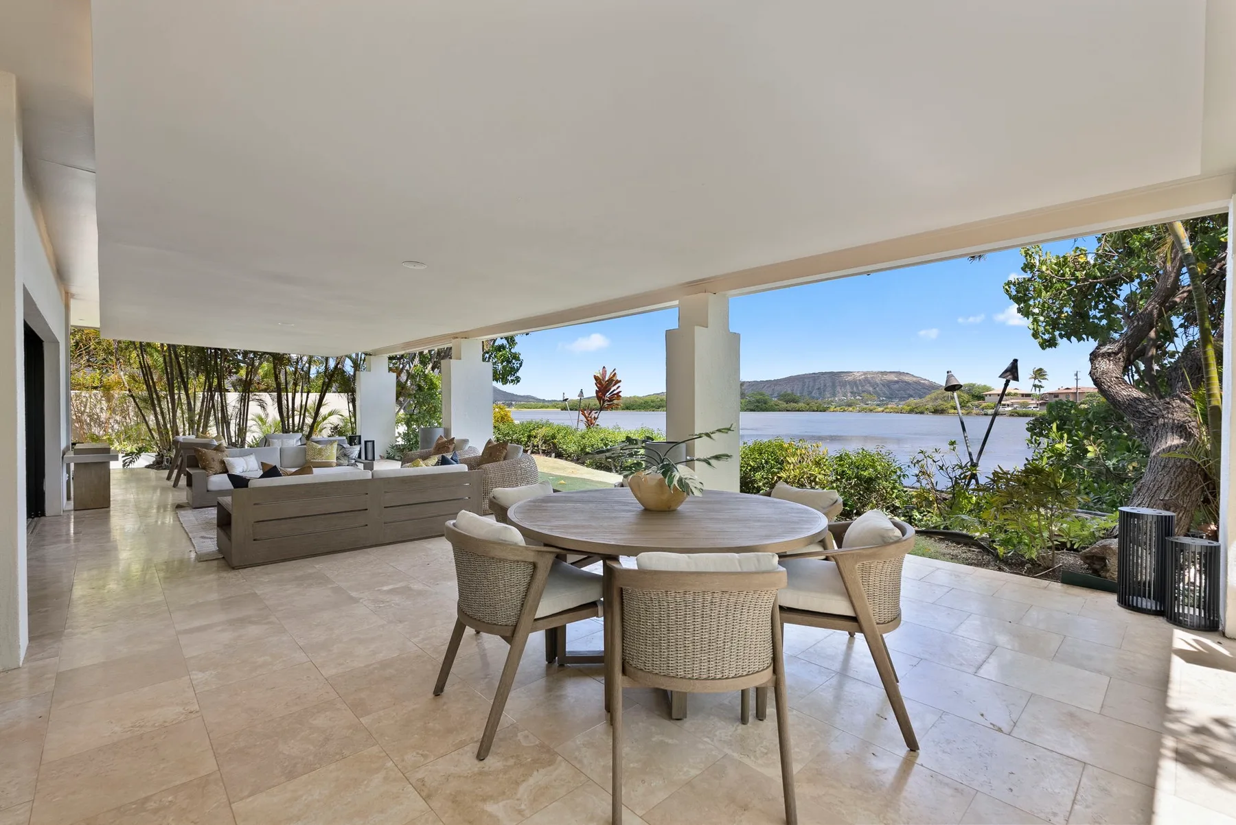 An open covered dining area overlooks a lake, with a round table and surrounding seating.