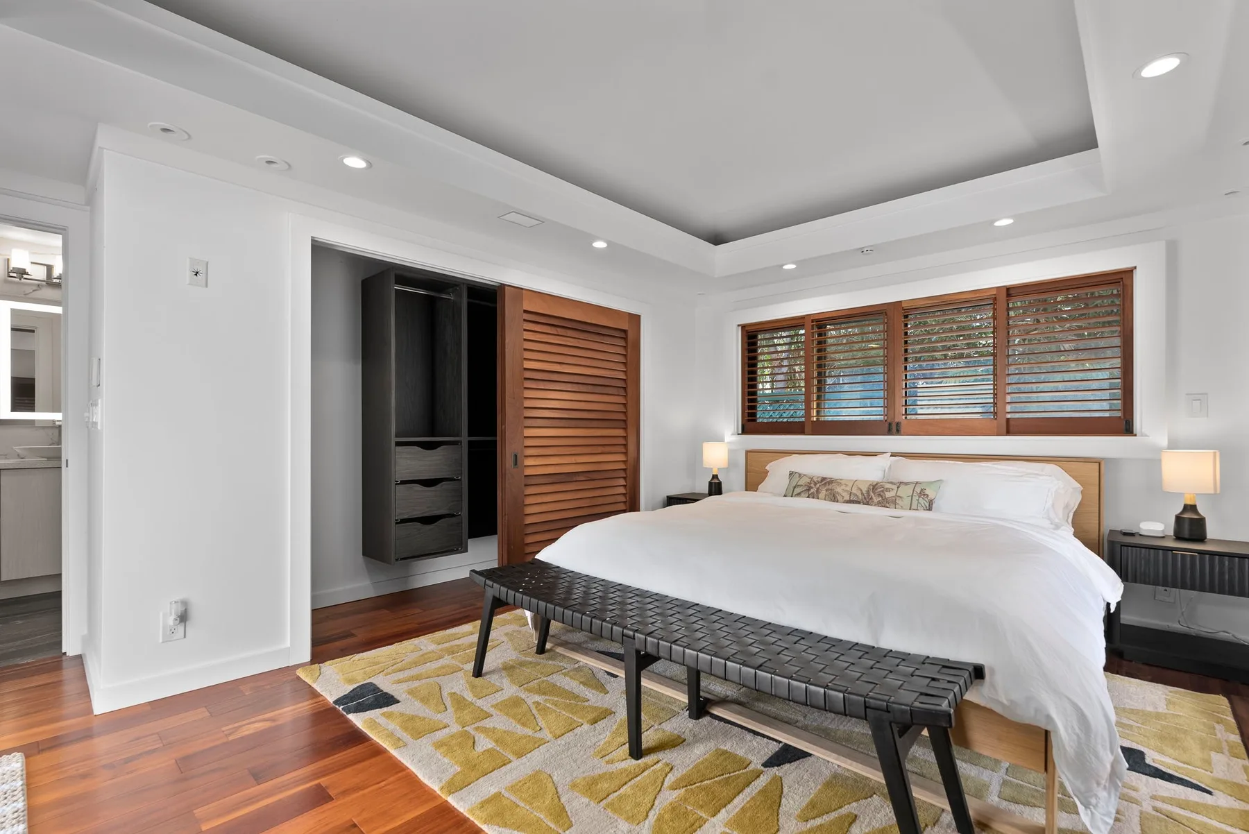 A bright bedroom with a large bed, a bench, and a window with wooden shutters.