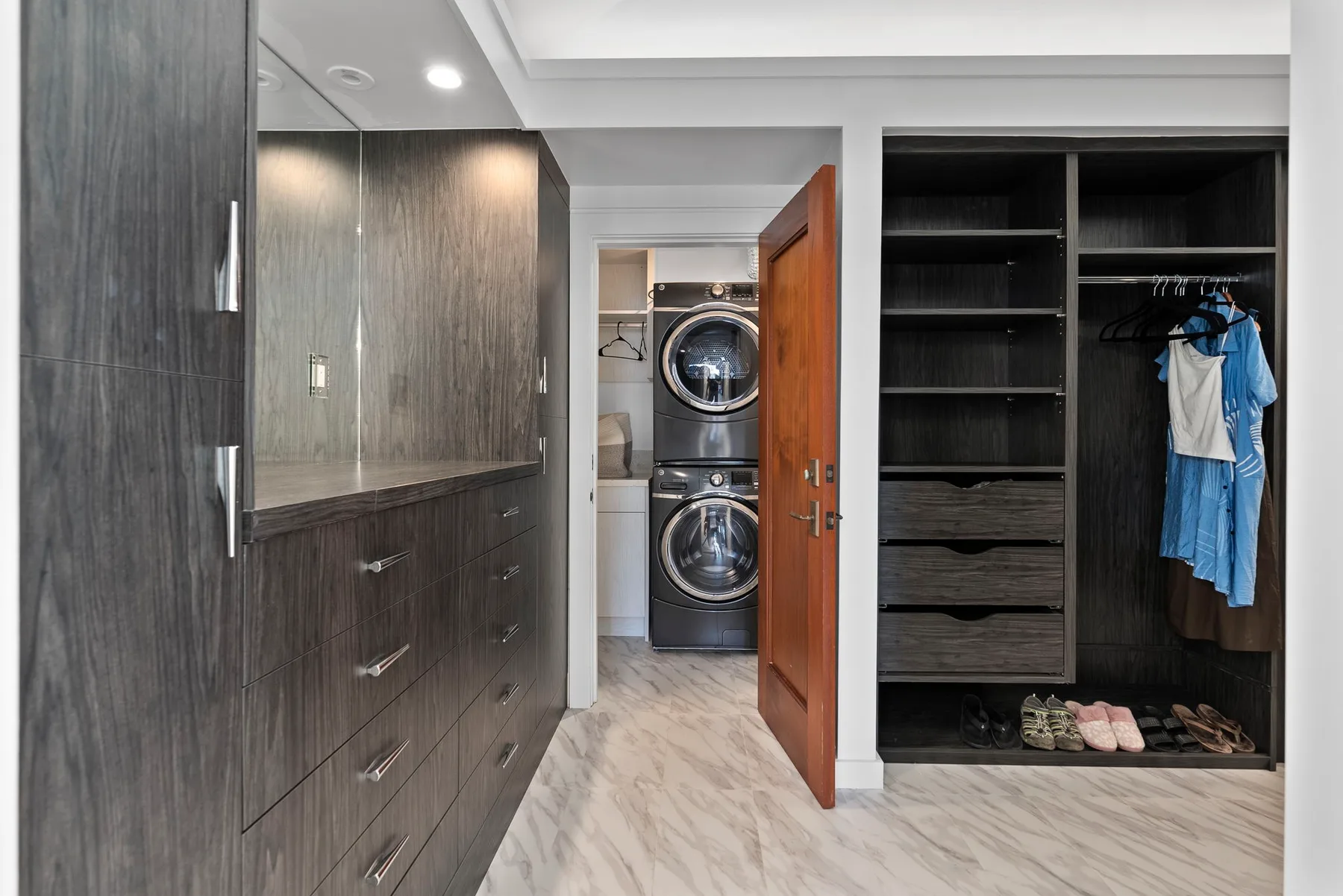 A dressing area with dark cabinetry and an open closet beside a laundry alcove.