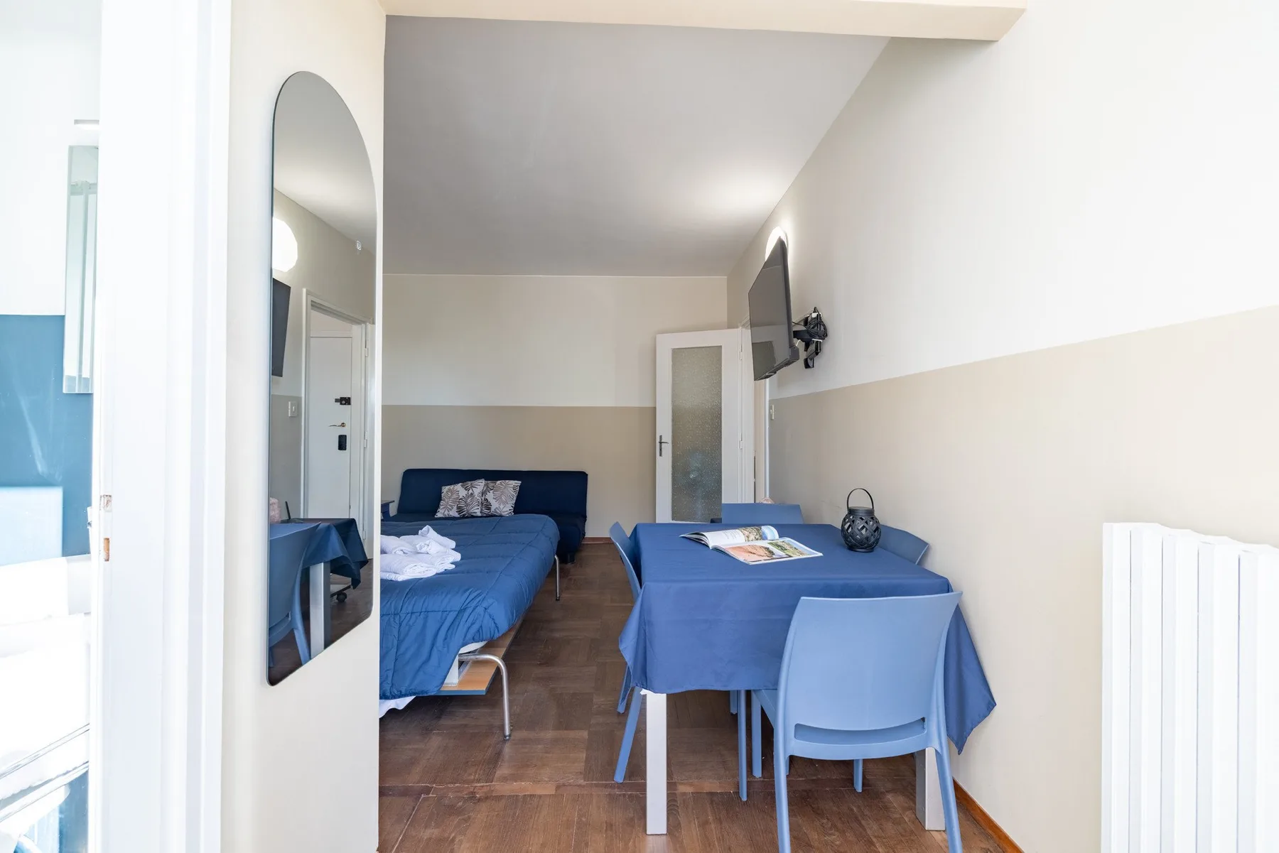 A compact room has blue seating, a table, and a wall-mounted television.